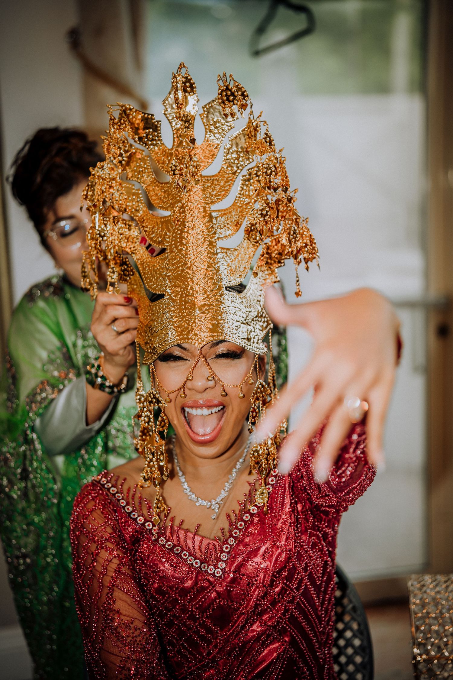 A joyful figure wearing an ornate golden crown headdress and sparkling red traditional Indonesian wedding attire.