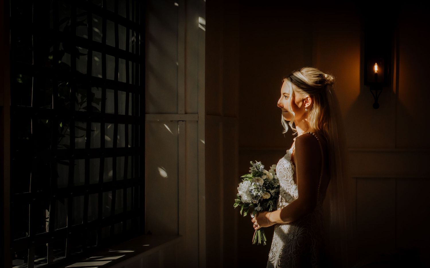 Moody sunlit hallway showing a person in wedding attire standing near a window.