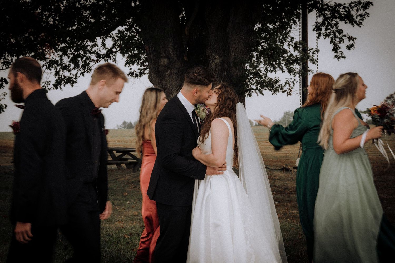 Wedding party members in formal attire gather outdoors for a celebration at sunset.