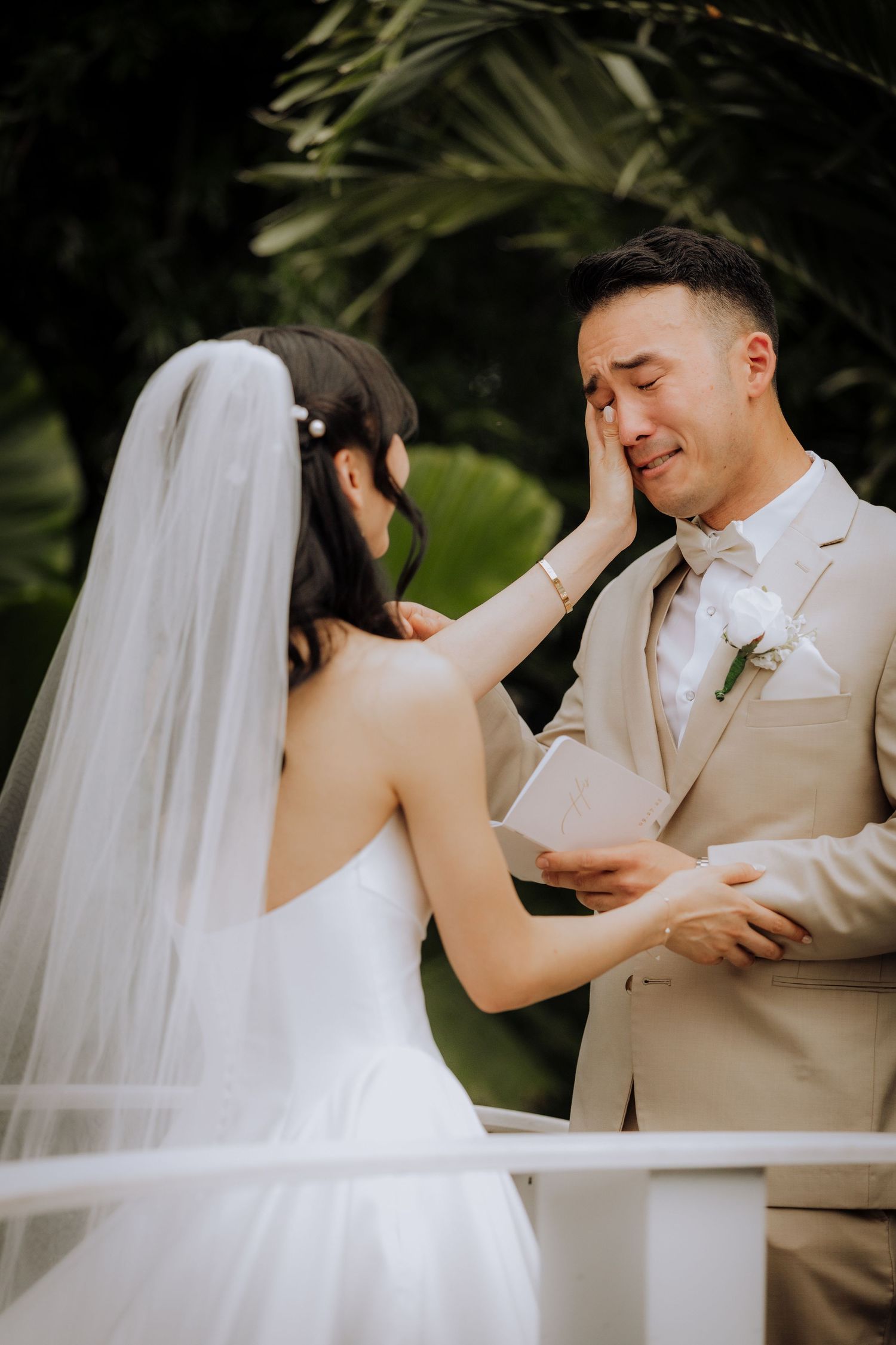Intimate wedding couple moment captured against tropical foliage backdrop.