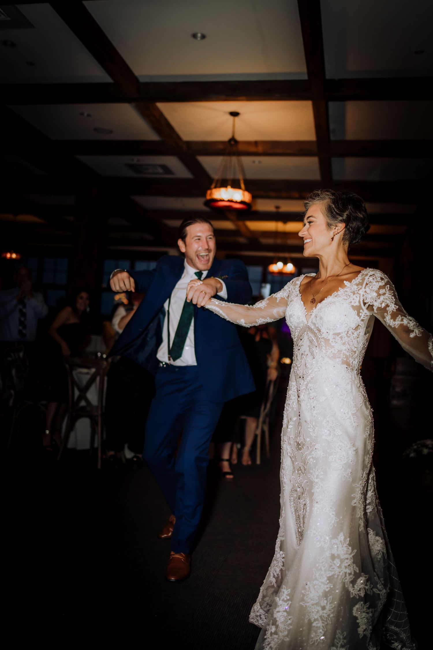 A joyful couple dancing together at their wedding reception in a rustic venue with wooden beams.