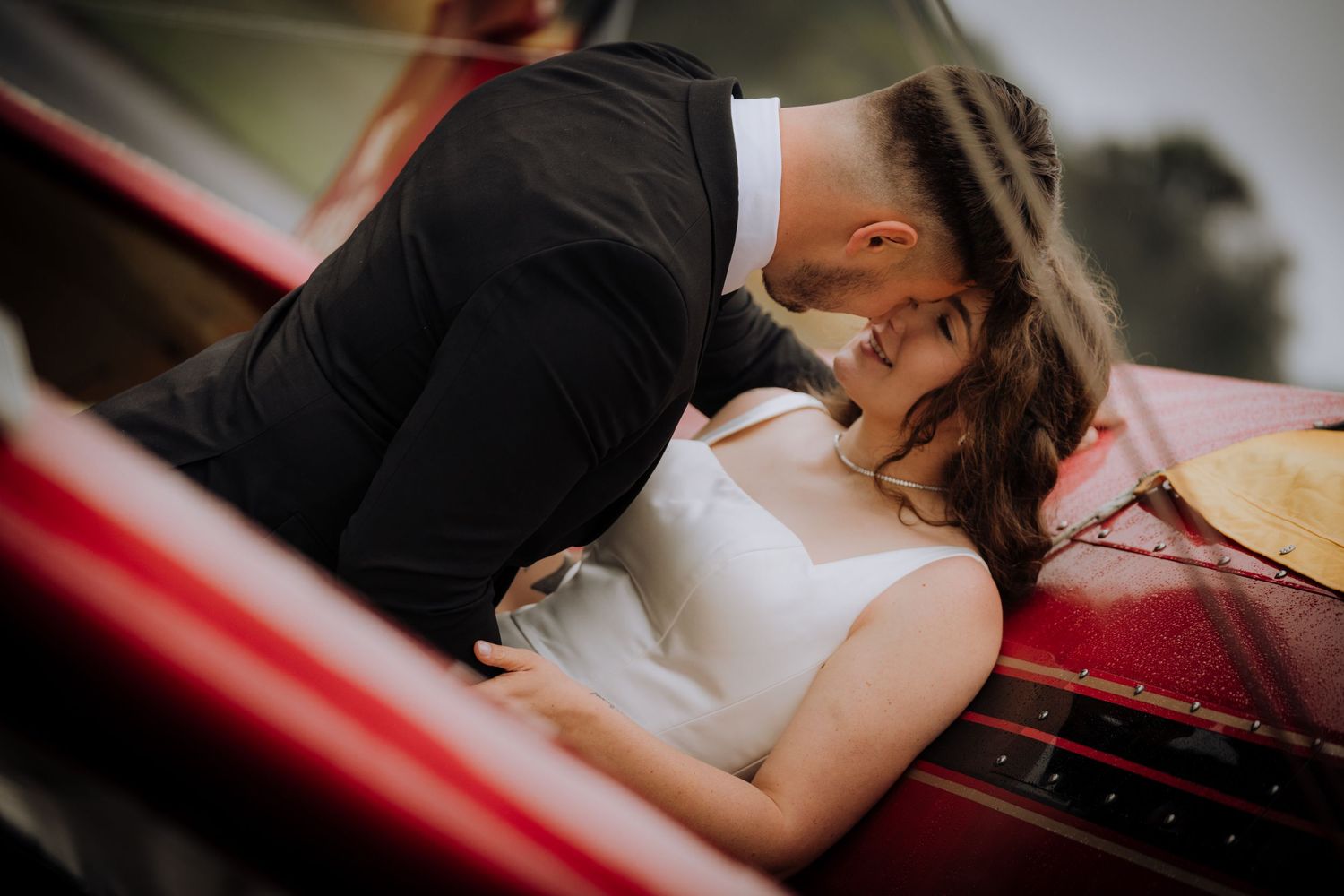 Couple sharing a romantic moment in a vintage red car during their wedding photoshoot.