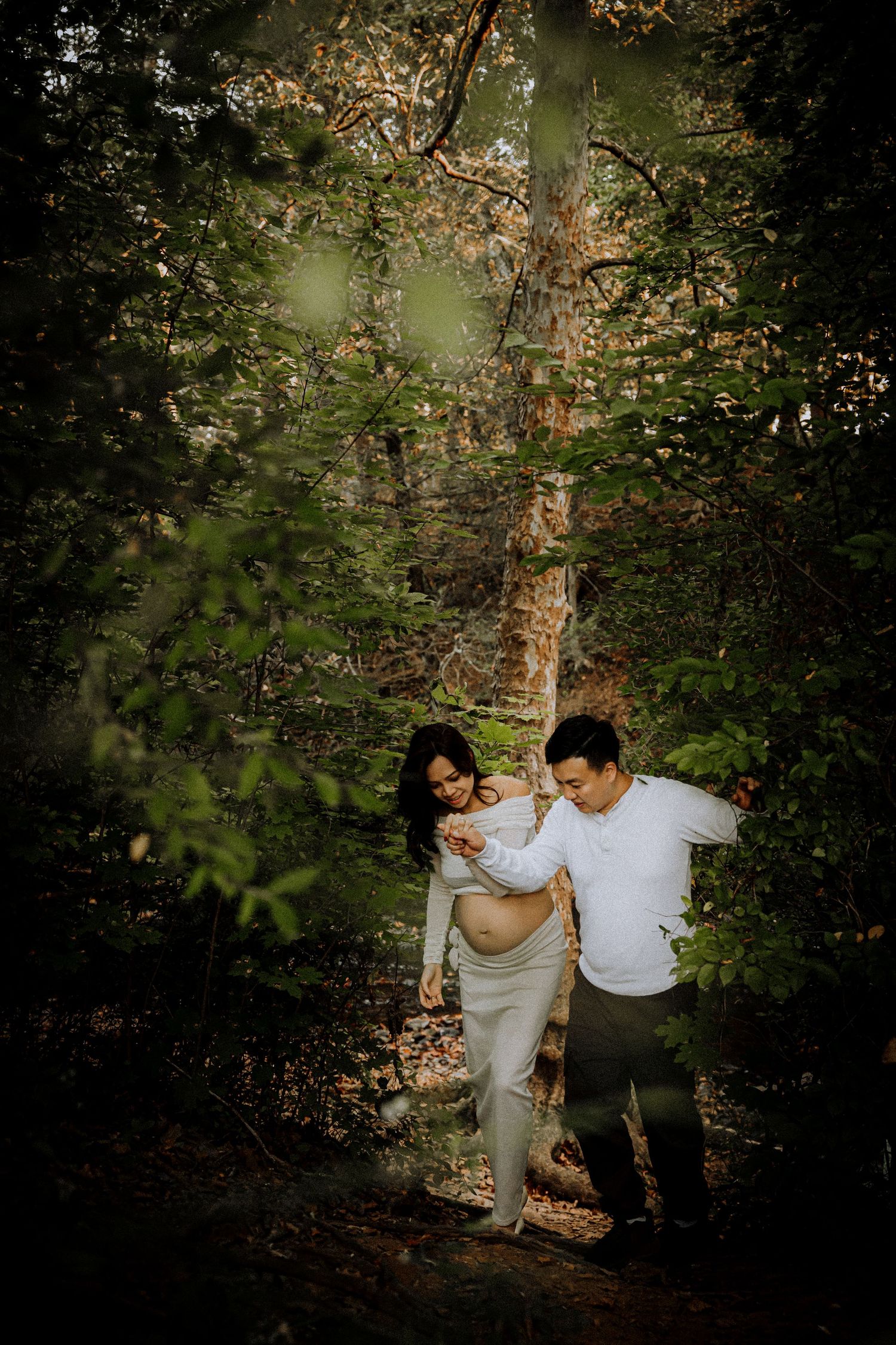 Couple walking together through a wooded area with dappled sunlight filtering through trees.