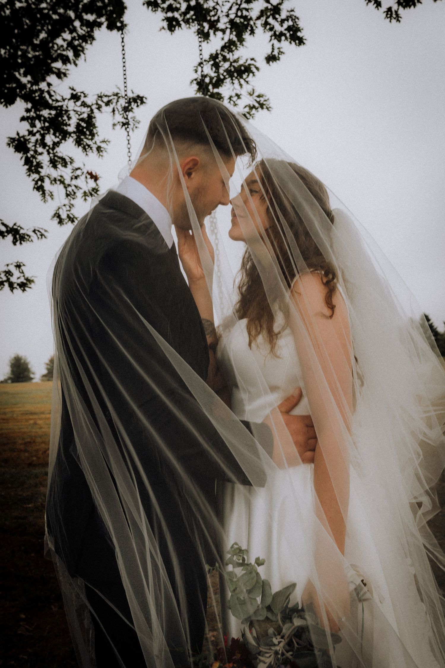 A romantic wedding moment captured through a flowing white veil in soft natural light.