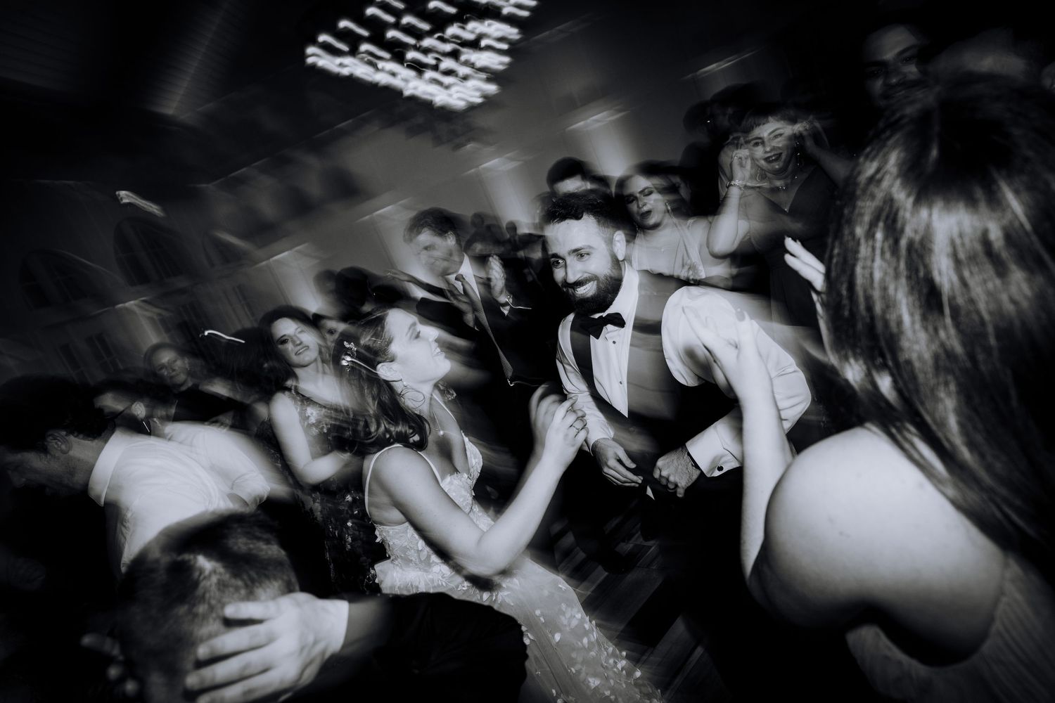 Motion-blurred black and white photo of wedding guests dancing at reception.