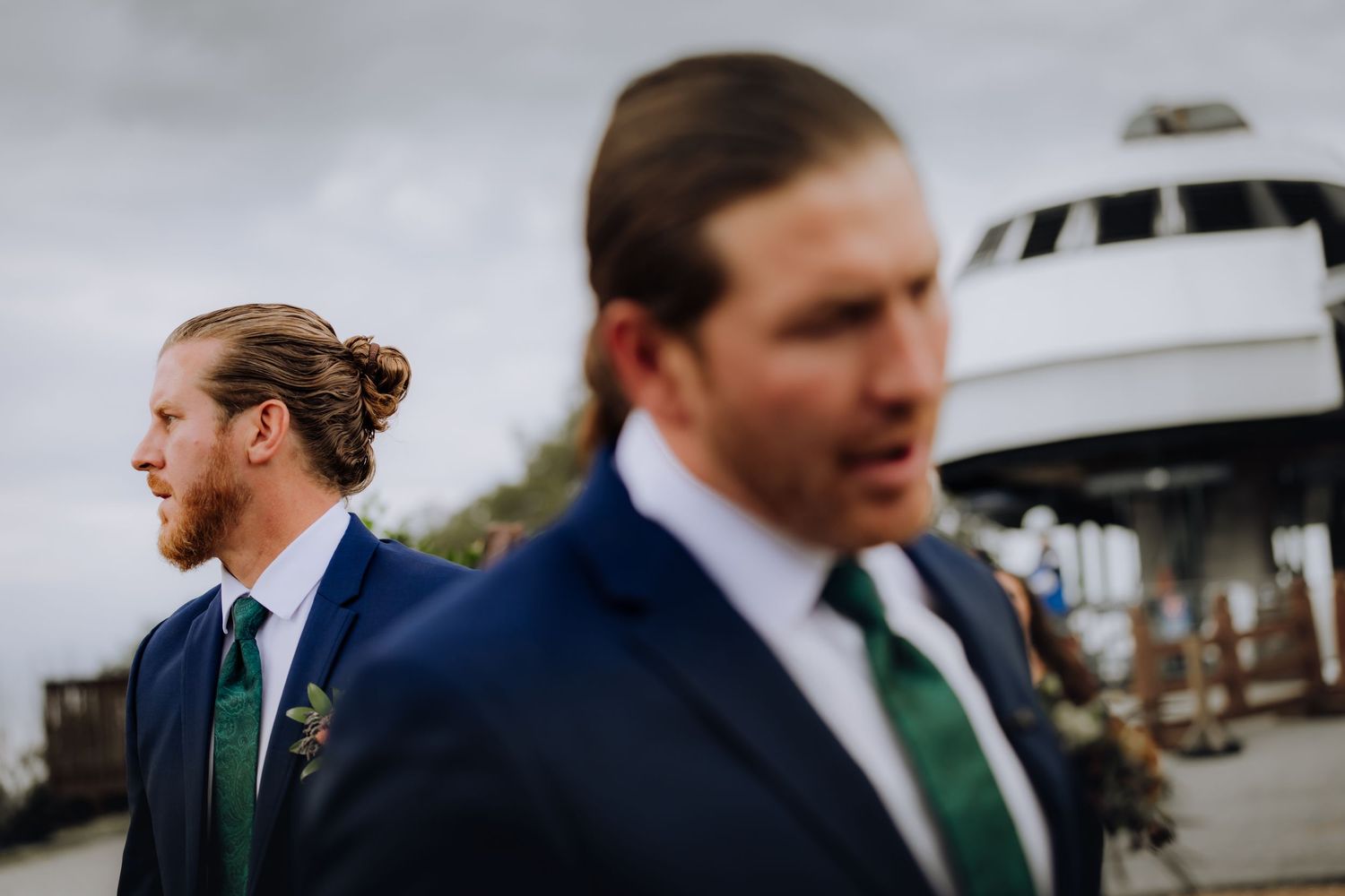 Two groomsmen in suits with green ties photographed with selective focus.