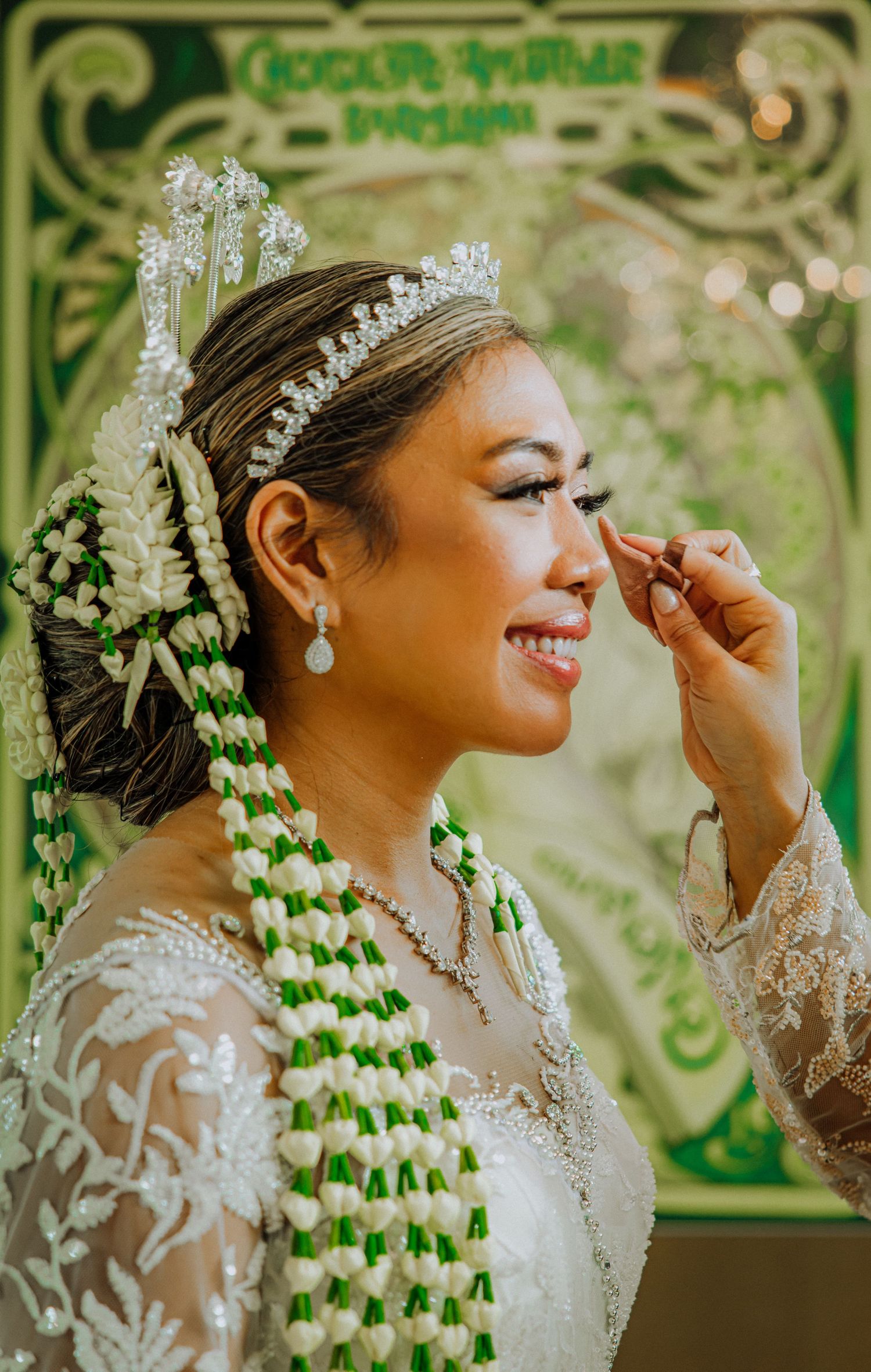 Wedding photographer captures elegant bride wearing white lace dress and sparkly tiara during final makeup touches.