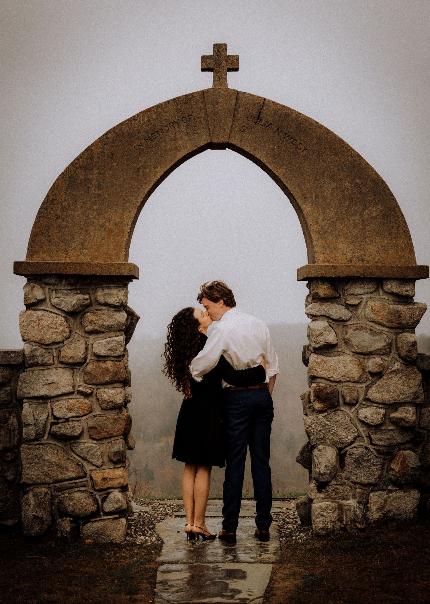 Couple posing playfully under stone archways with cross detail.