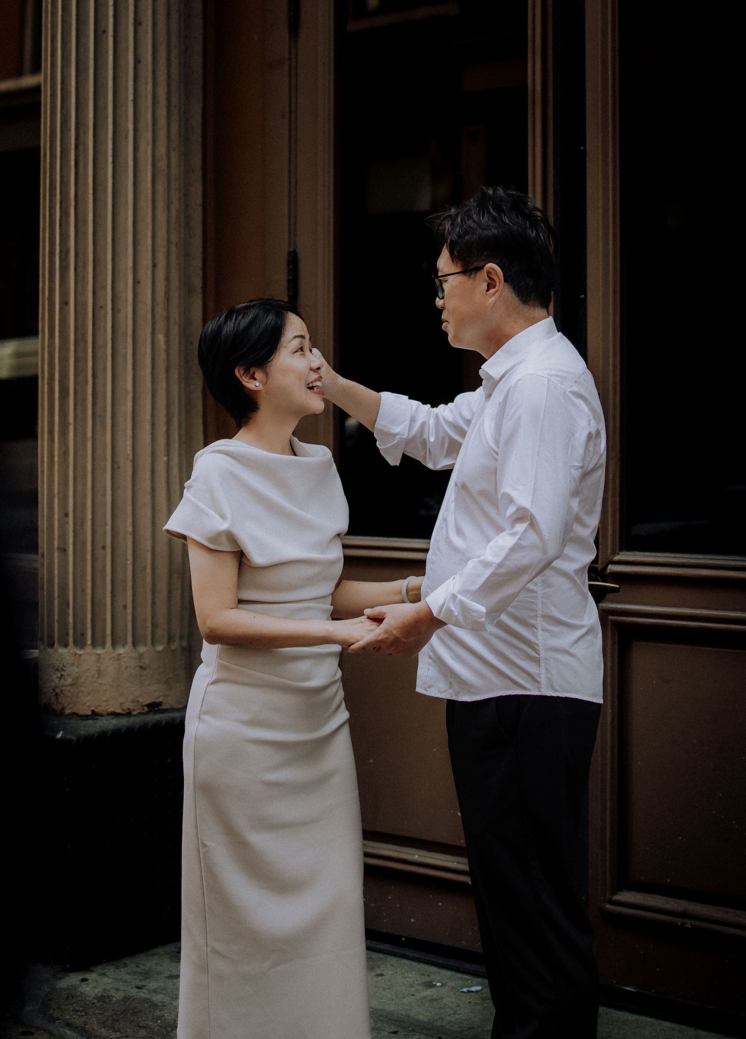 People in white clothing pose and interact in front of a building with classical architecture.