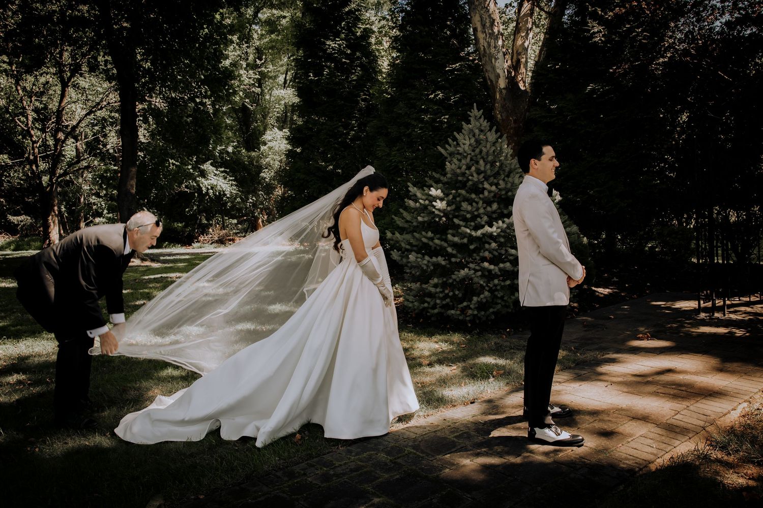 A romantic wedding moment captured in a wooded outdoor setting with flowing white dress and veil.