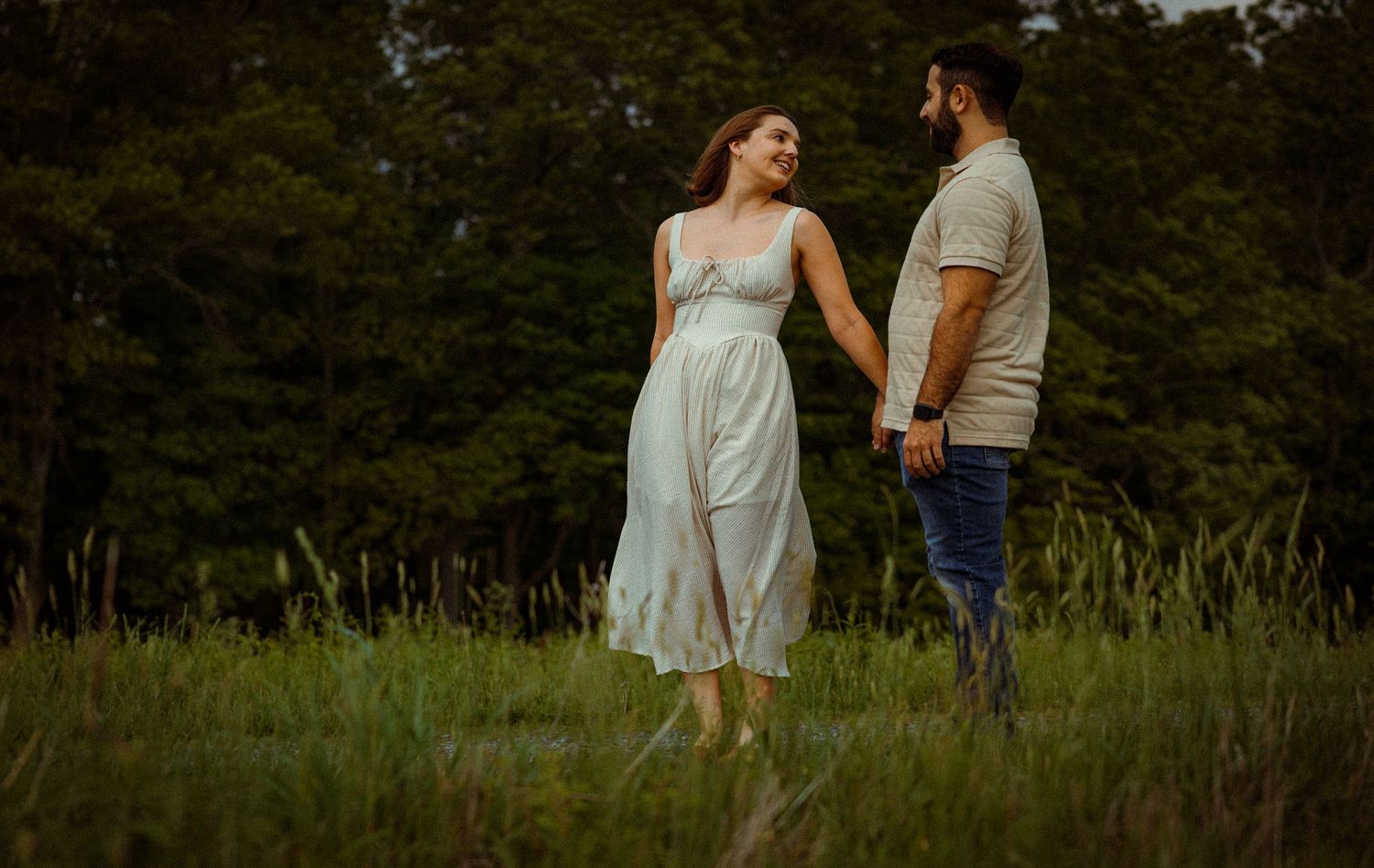 Couple walking hand in hand through a scenic meadow at sunset.