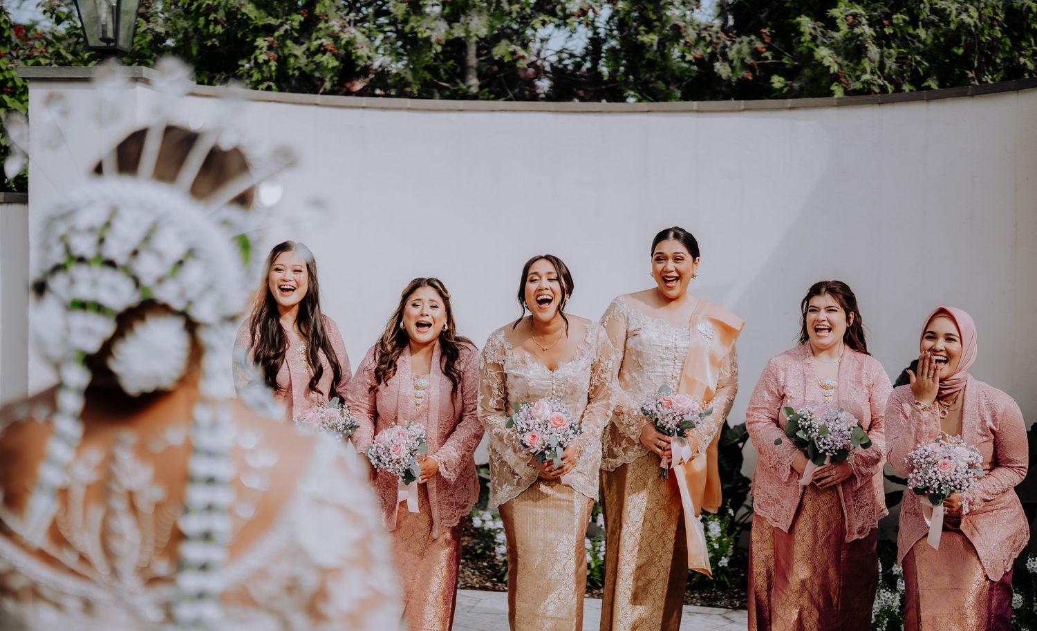 A group in flowing pink dresses laughing together during an outdoor celebration.