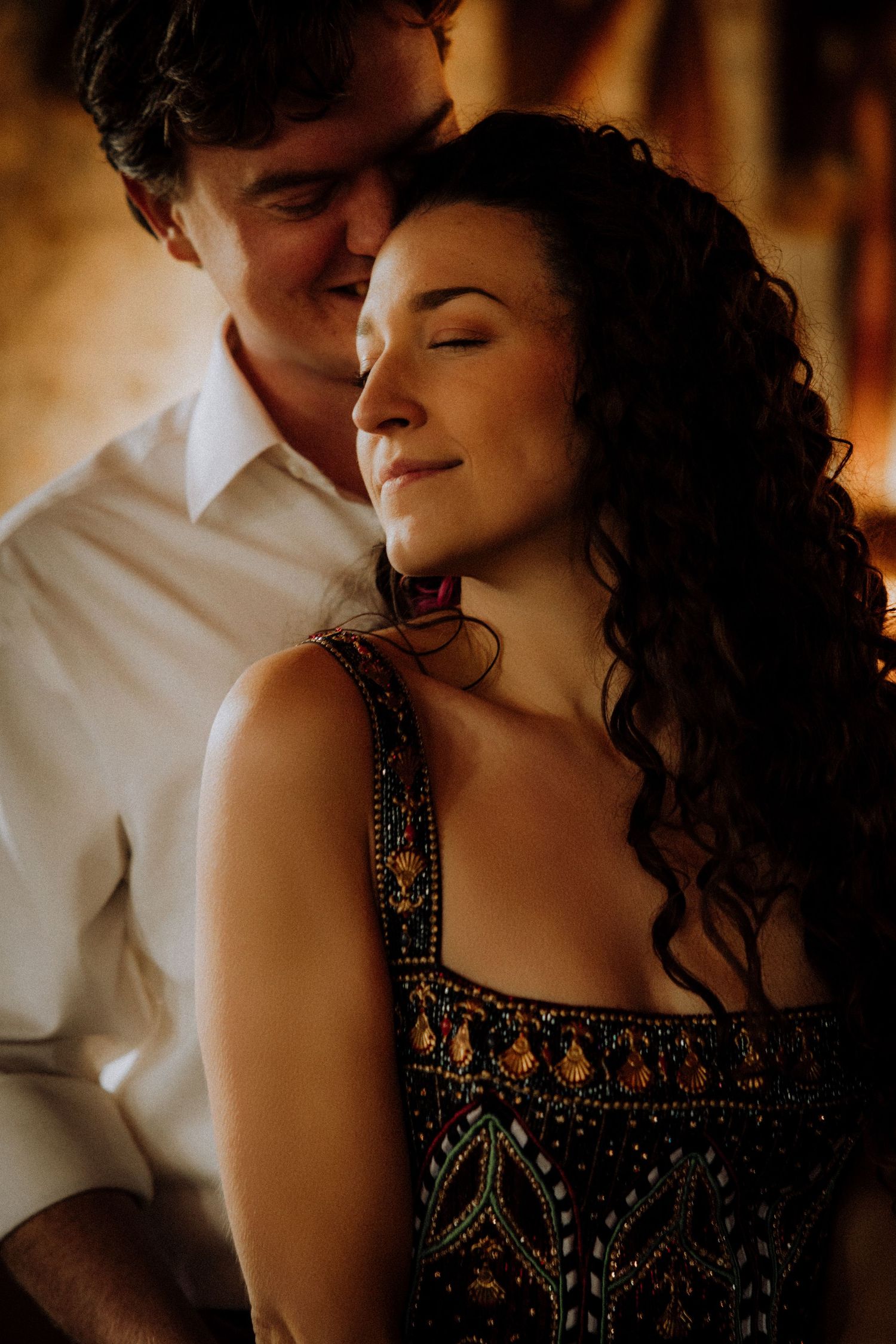 Romantic couple sharing an intimate moment in warm lighting with a black embellished dress.