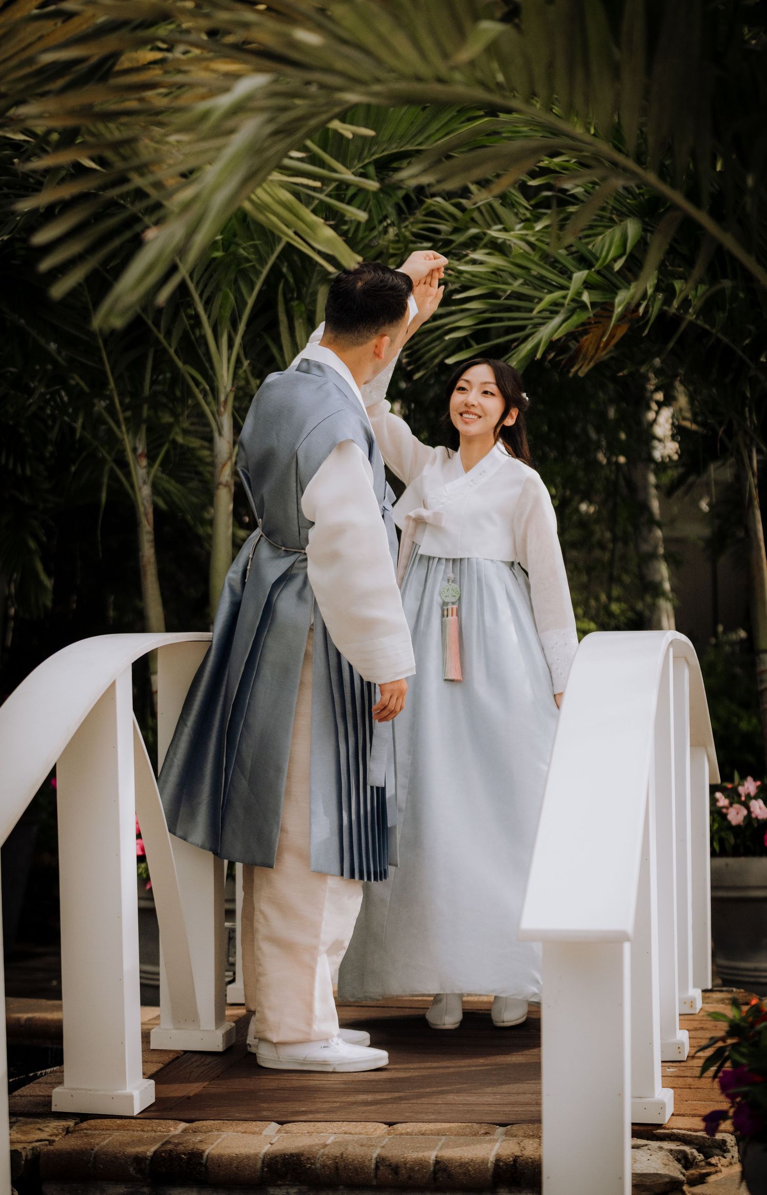 Traditional Korean hanbok wedding ceremony in a garden setting with palm trees.
