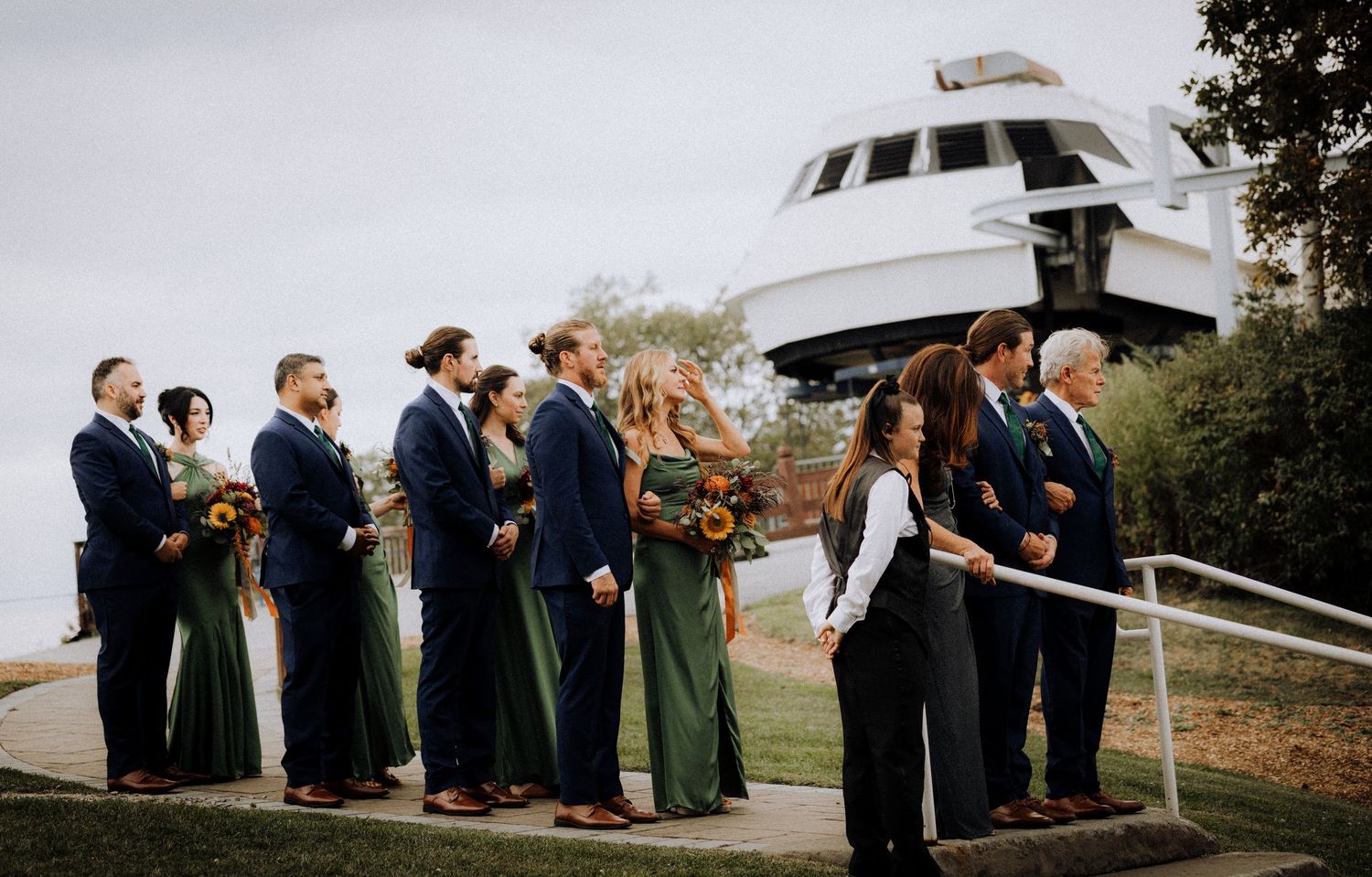 Wedding party stands in line against scenic mountain backdrop on outdoor terrace.