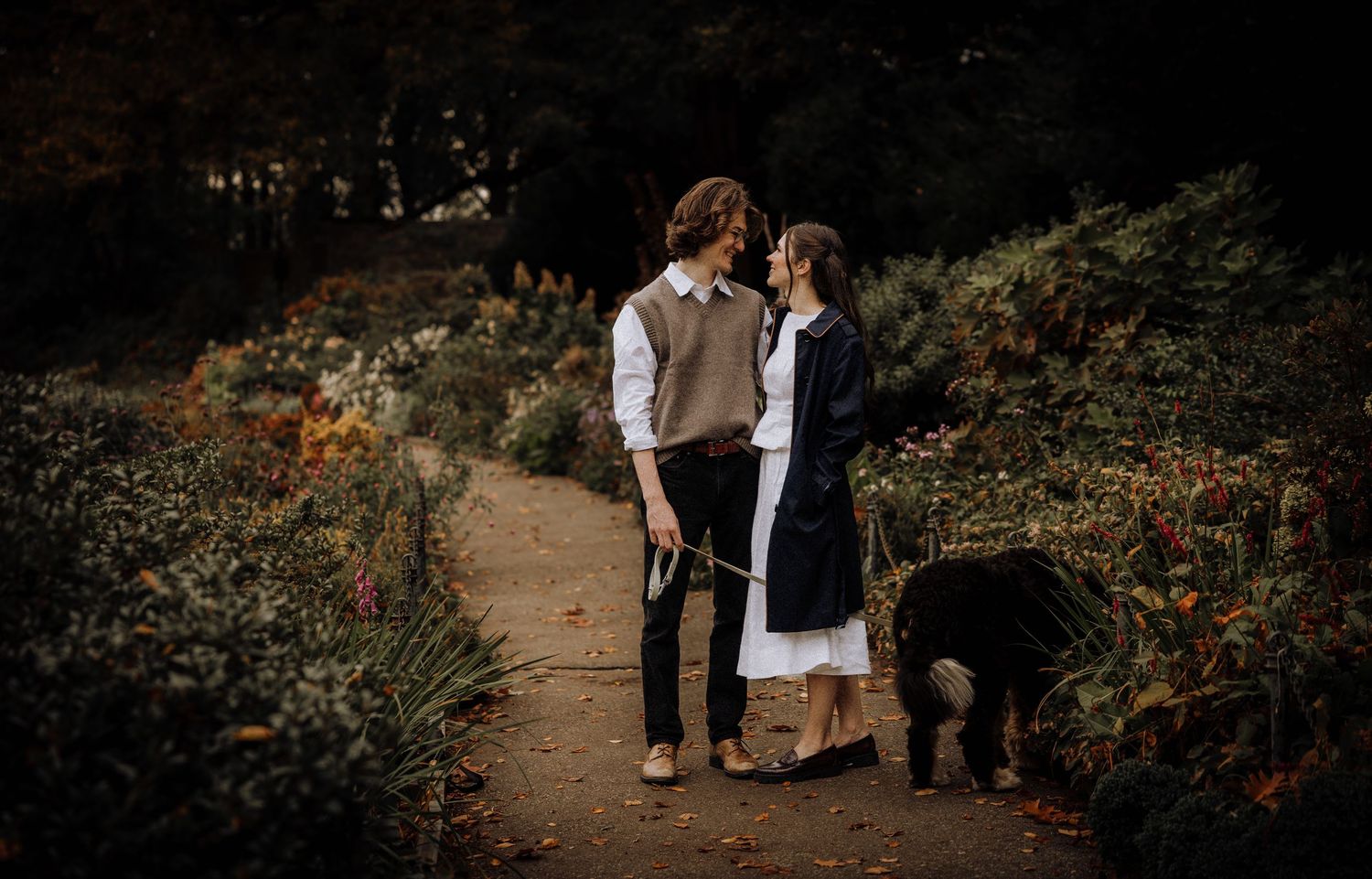 A romantic forest pathway lined with trees and autumn foliage creates a dreamy outdoor setting.