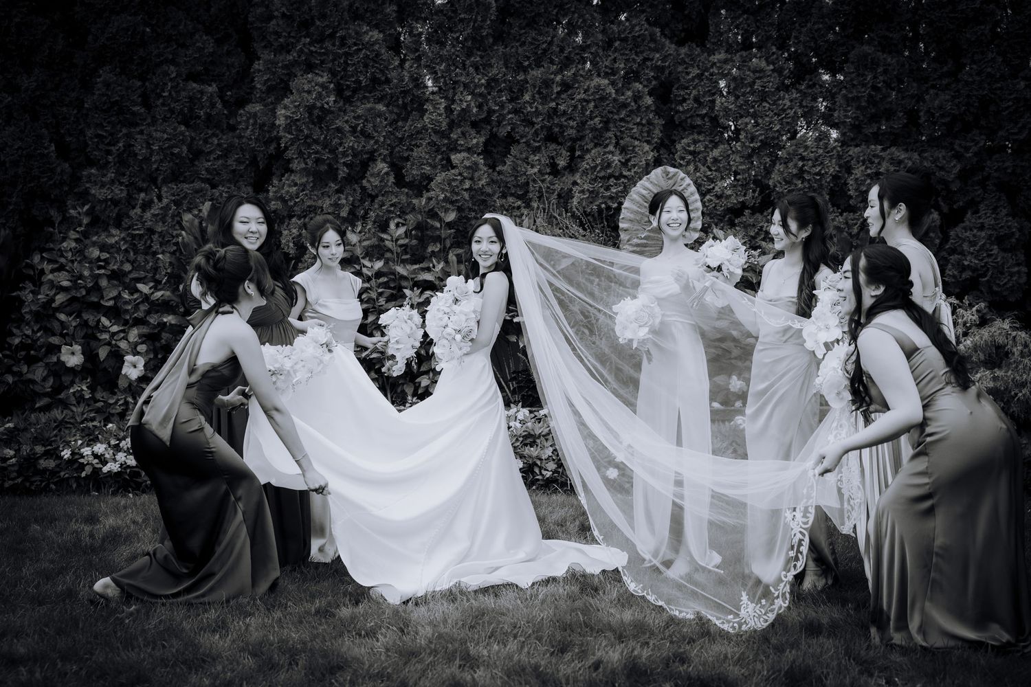 Wedding party seated on grass creating artistic composition with flowing white dress.