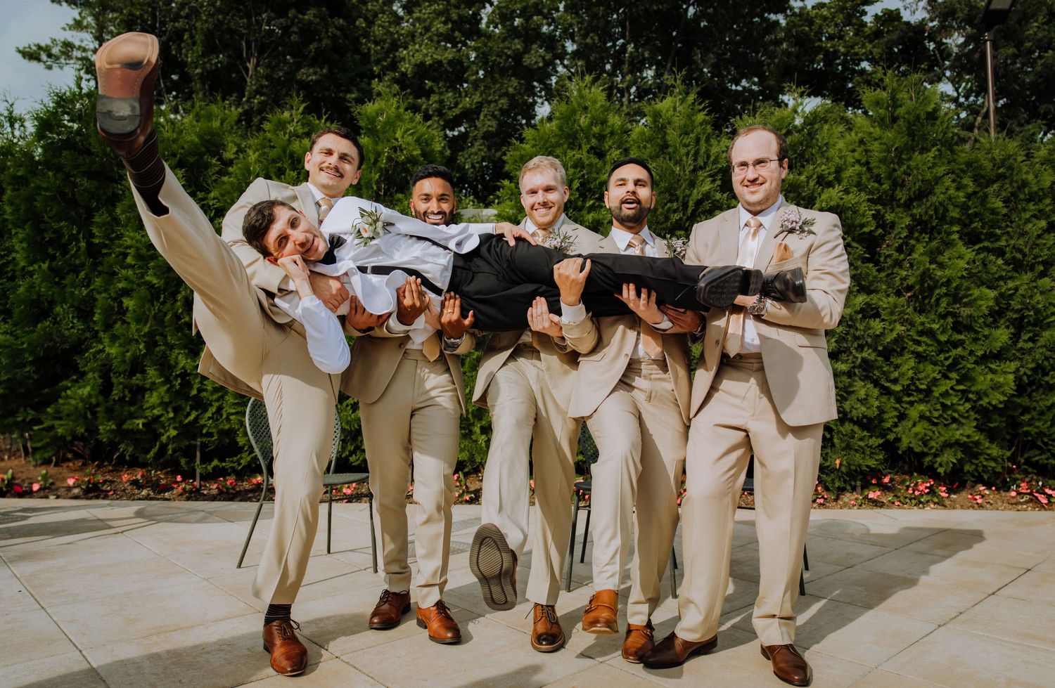 A lively group in beige suits and brown shoes strike playful poses outdoors on a sunny day.