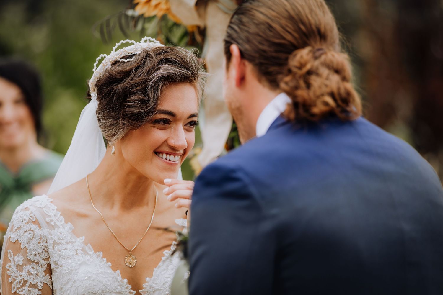 Close-up of bride in lace dress sharing intimate moment during outdoor ceremony.