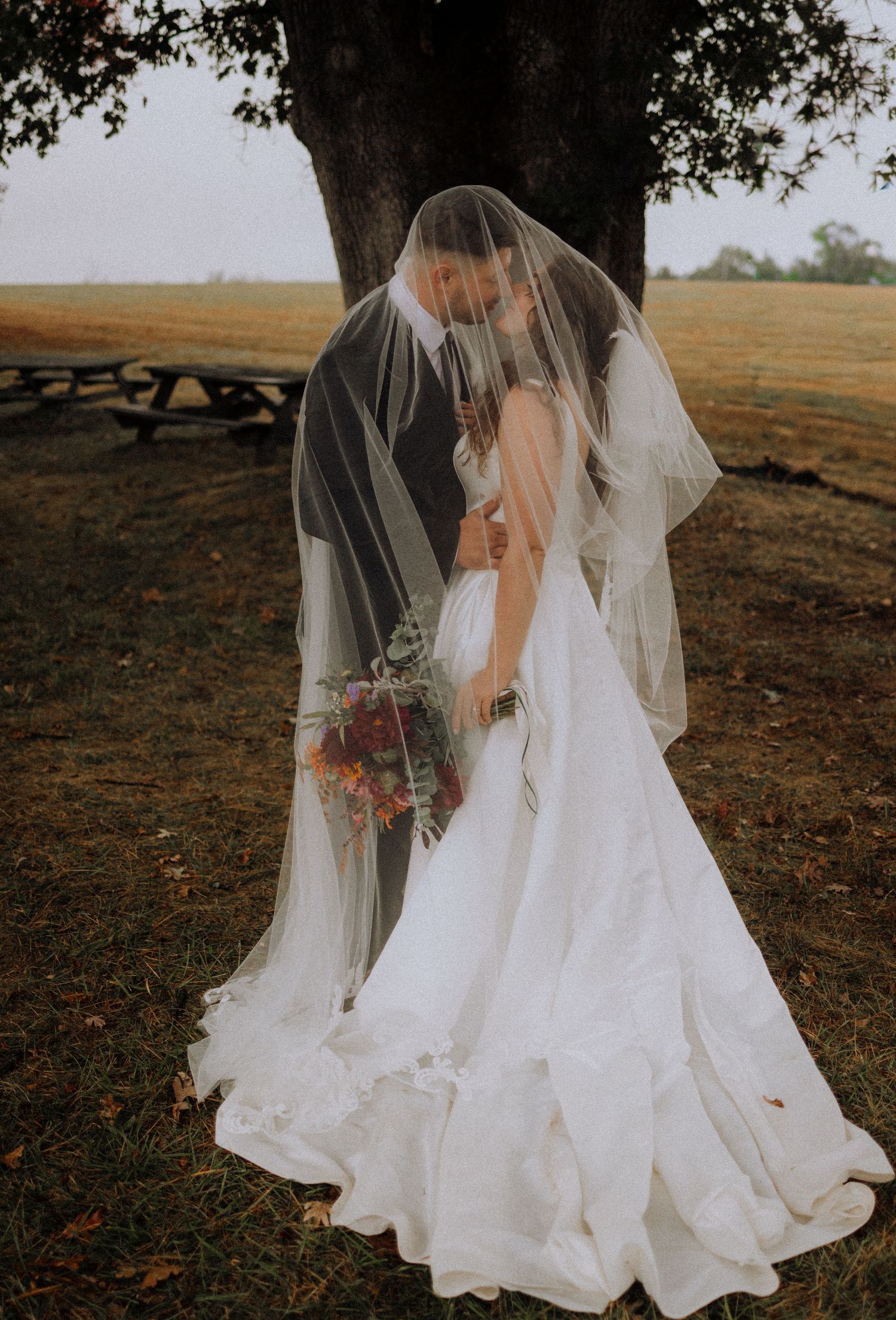 Romantic wedding portraits through sheer veil in golden outdoor setting.