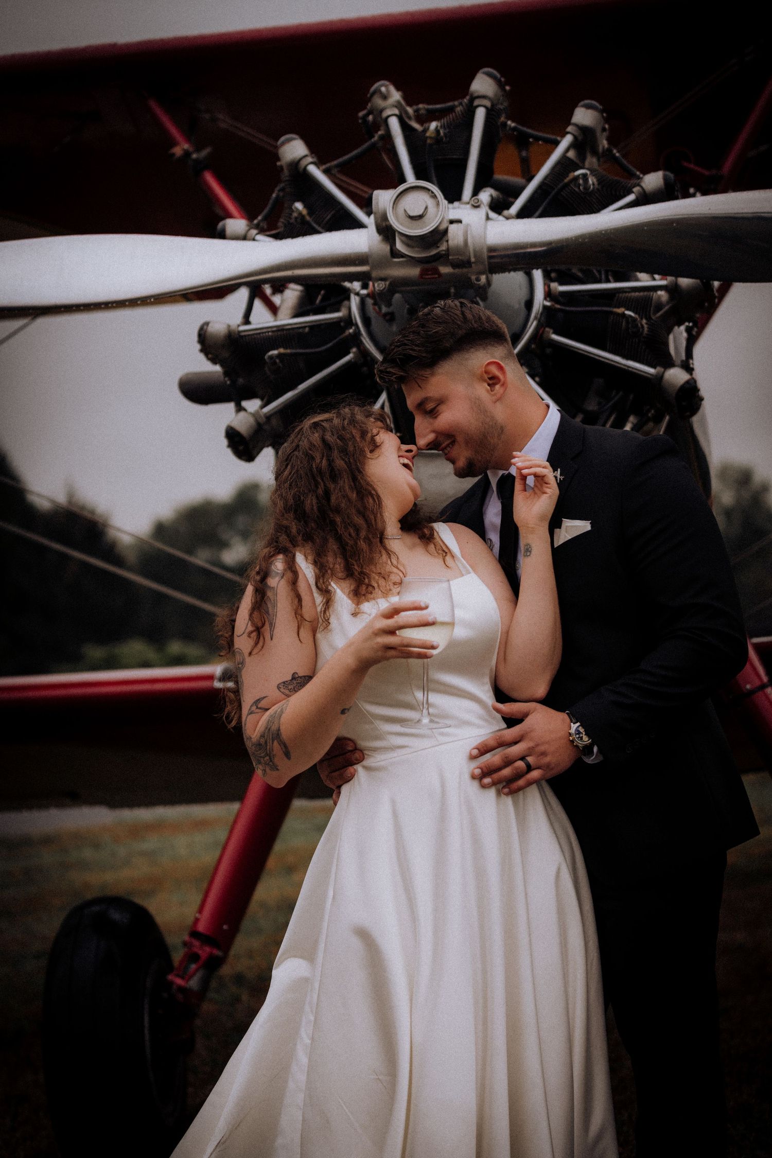 Romantic couple poses in front of vintage aircraft during wedding photoshoot.