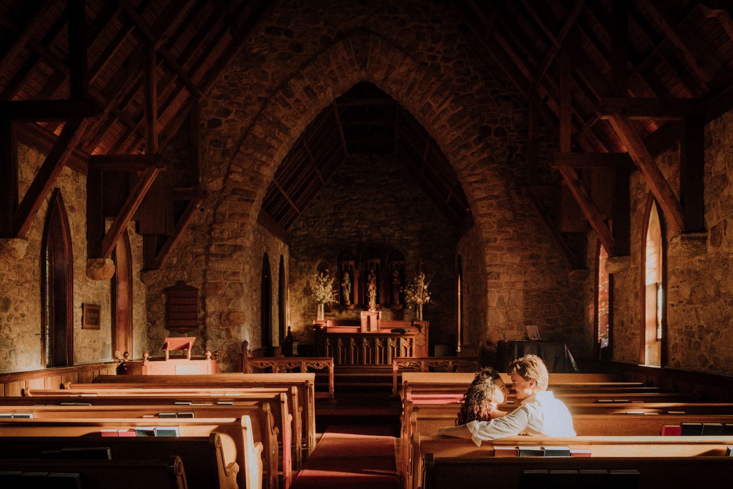 Stone church sanctuary with vaulted ceilings and rows of wooden pews in warm lighting.