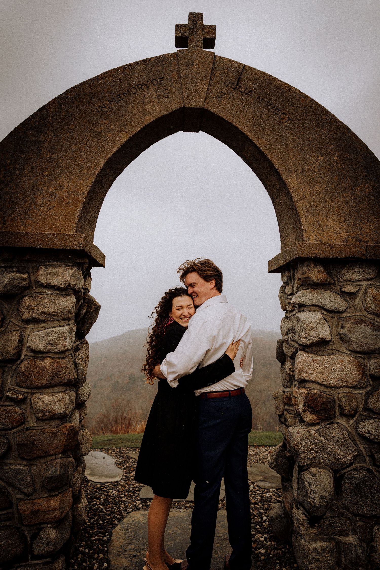 Couple embracing under stone archway against misty mountain backdrop.