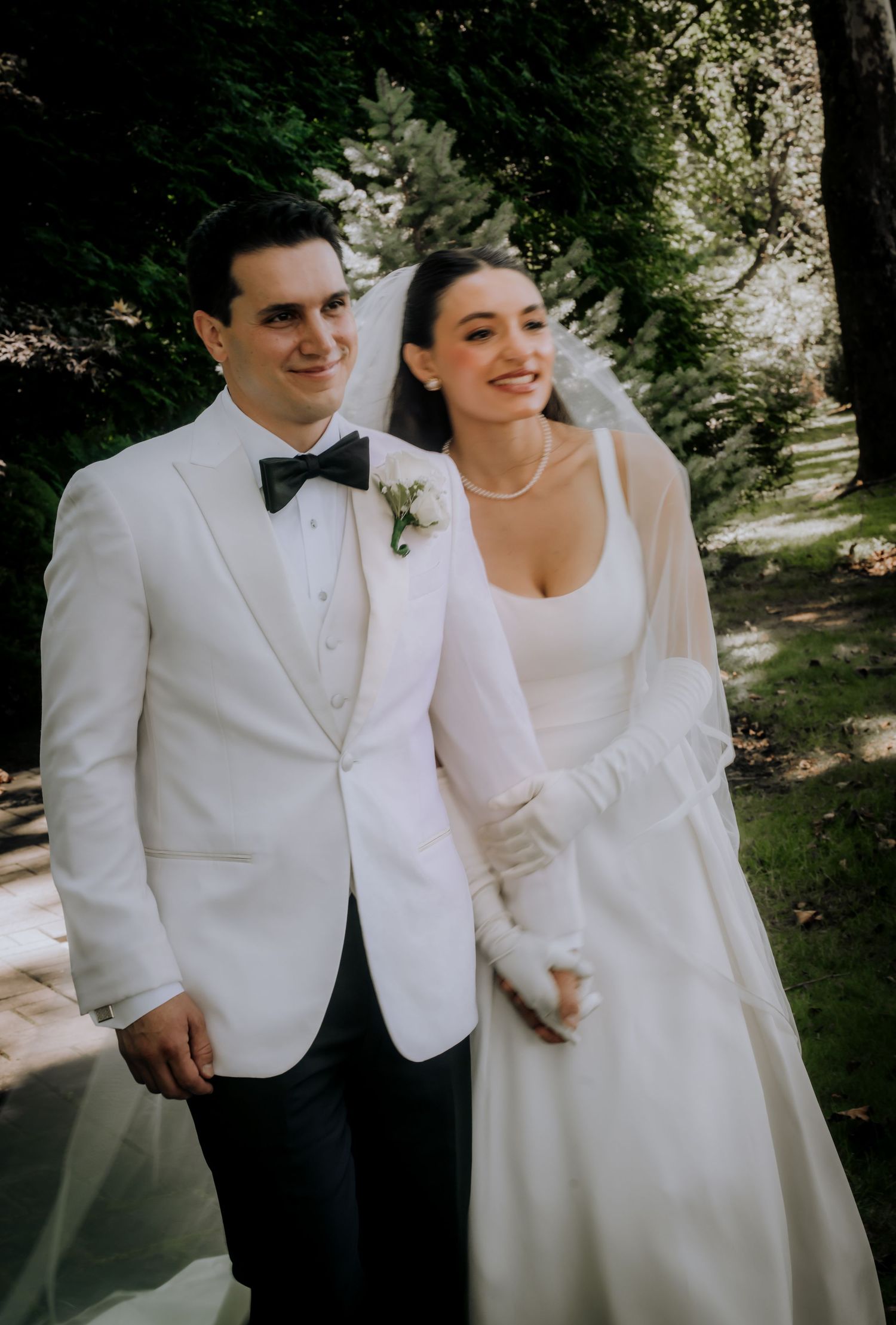 A couple in matching white wedding attire poses together in a garden setting.