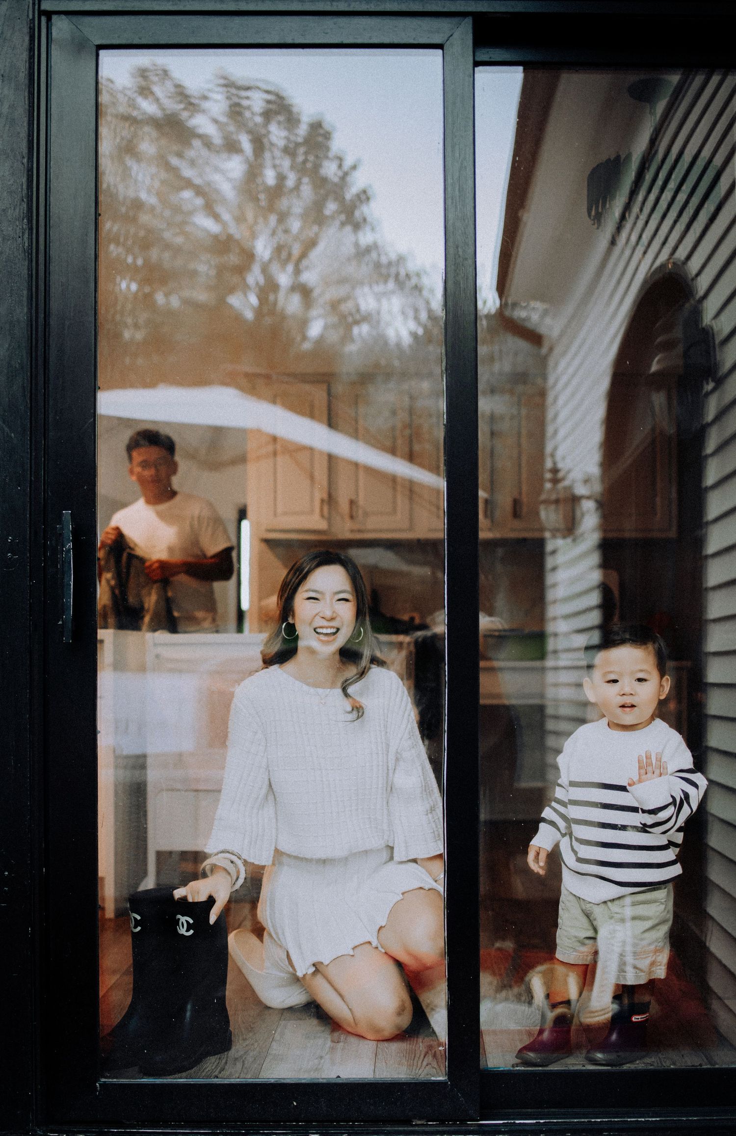 Through window panes, a joyful indoor scene with striped clothing and white decor is captured.