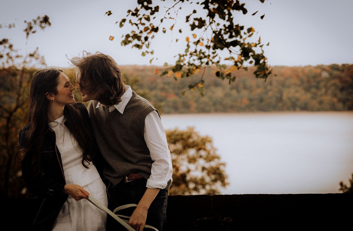 A couple shares a romantic moment in an autumn setting with golden leaves and natural light.