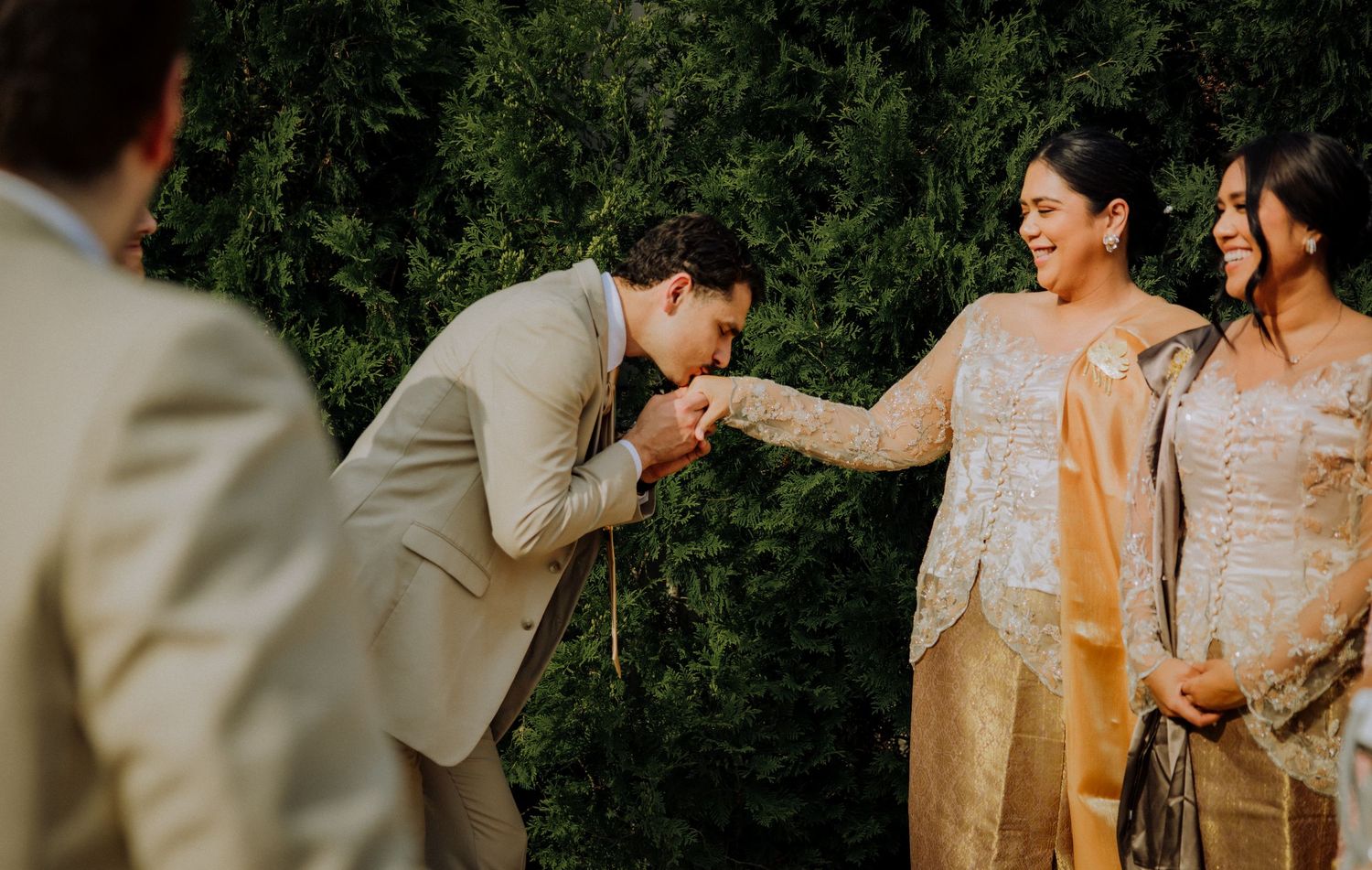 A traditional Indonesian wedding ceremony takes place outdoors as the groom bows gracefully to greet the bride.