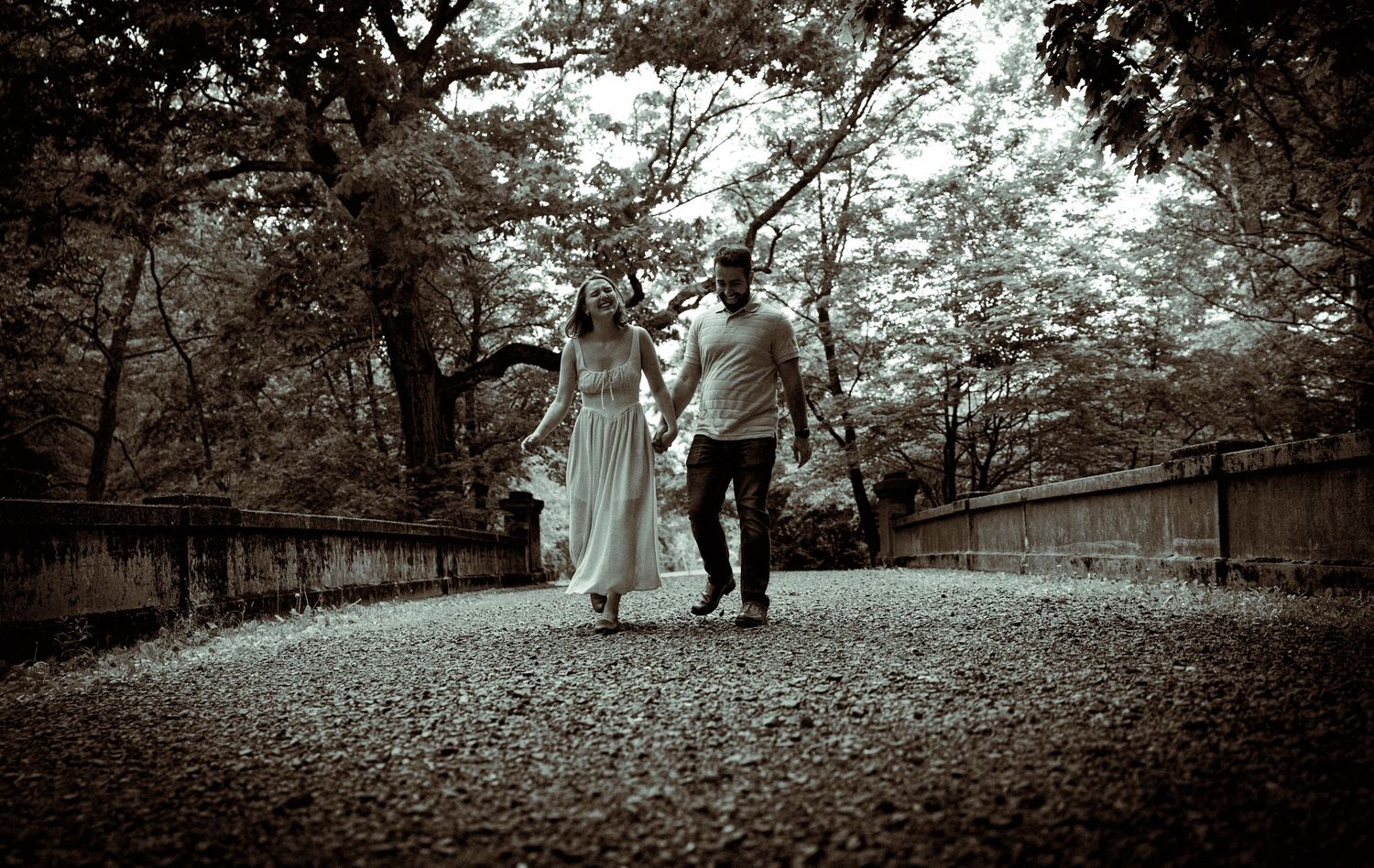 Black and white engagement photos taken on a winding forest path surrounded by trees.