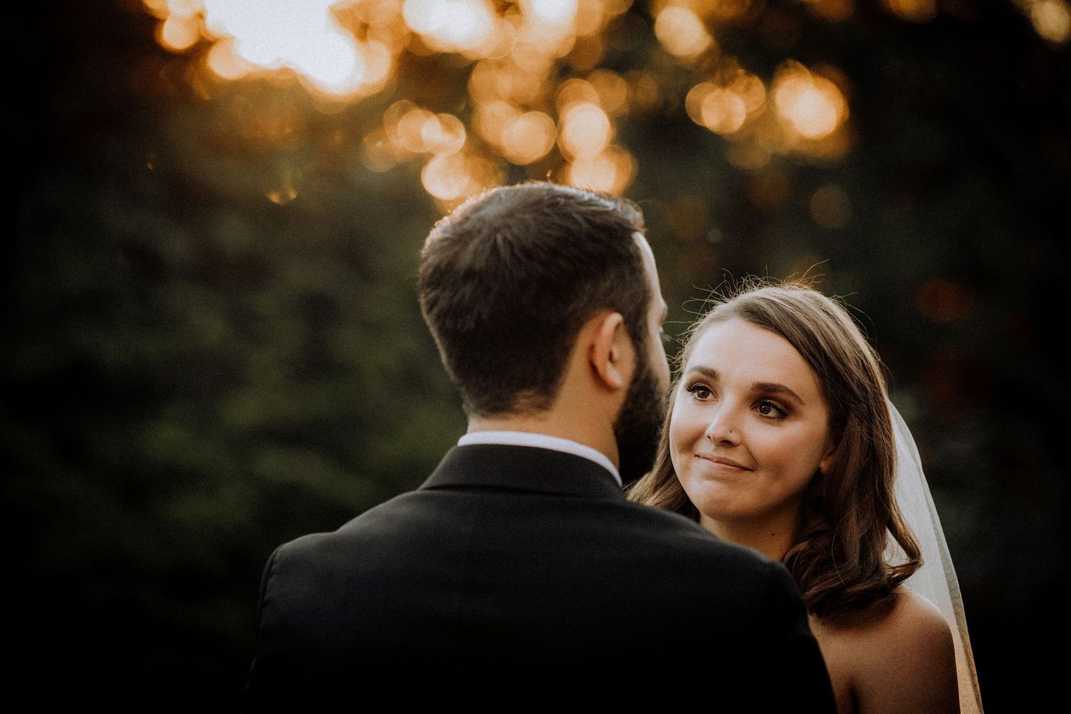 Golden sunset bokeh lights create a dreamy atmosphere at an outdoor wedding celebration.