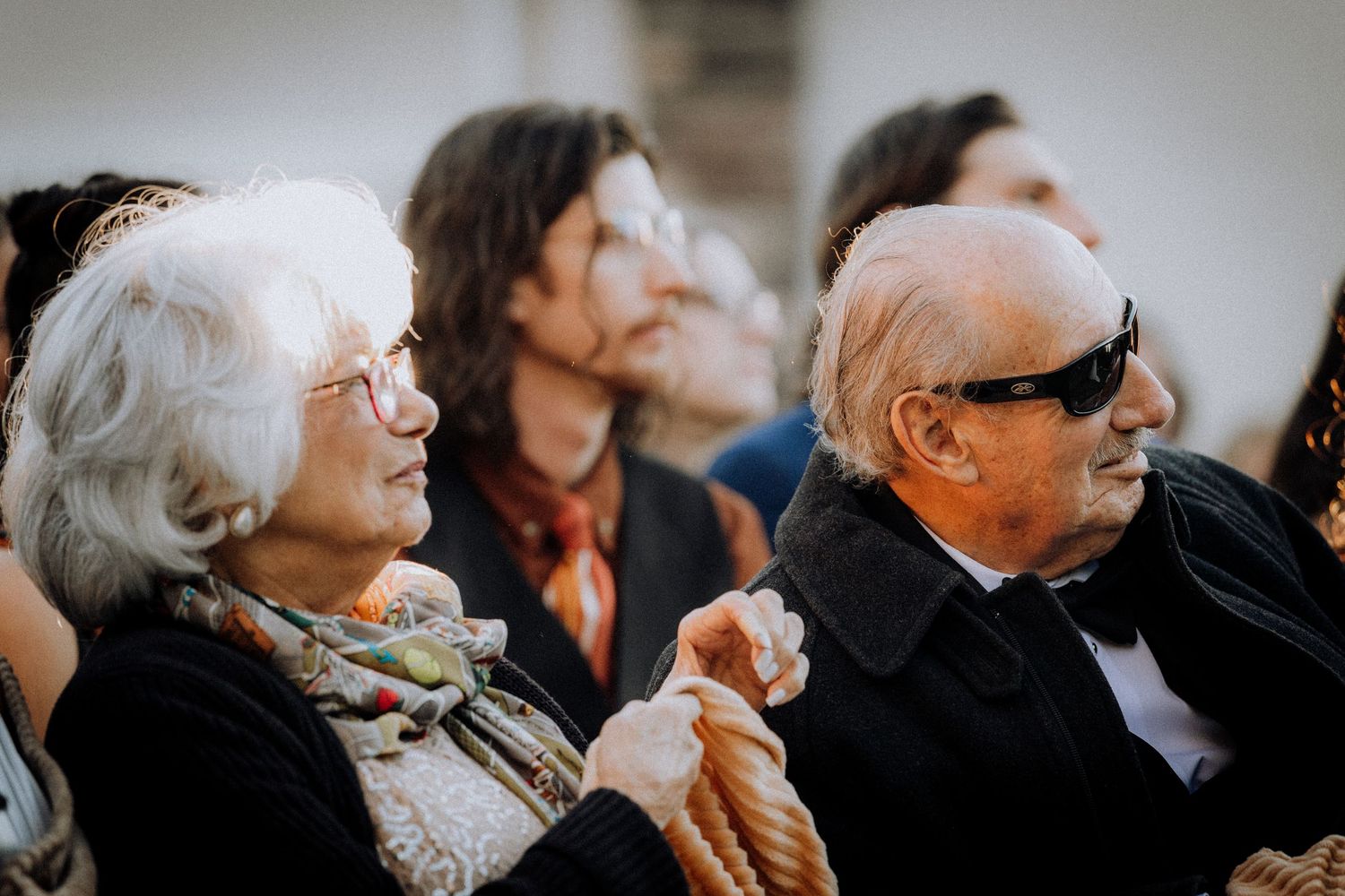 Elderly wedding guests seated in rows smile and look upward during an emotional ceremony moment.