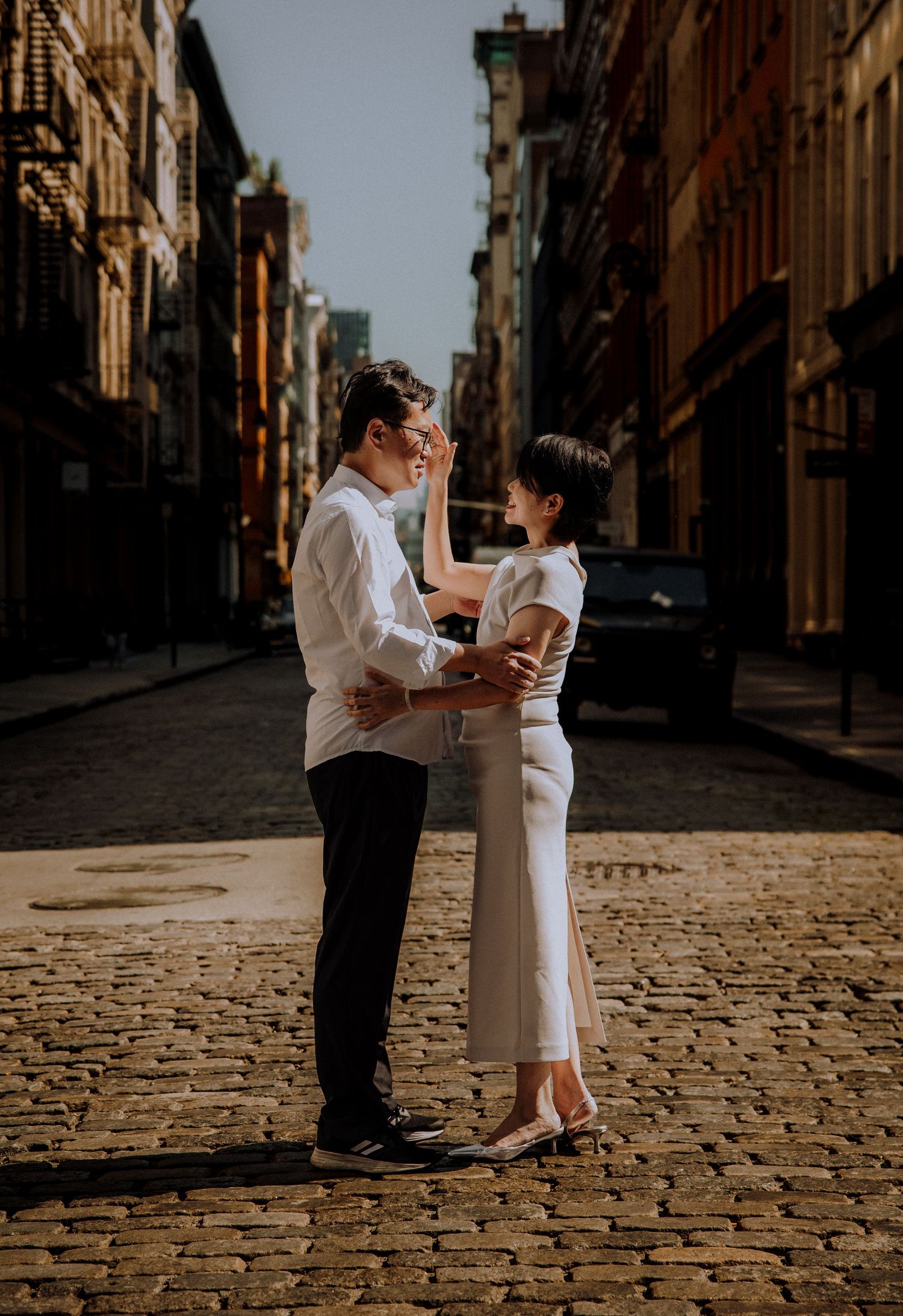 Couple dancing on cobblestone street in formal attire creates romantic vintage scene.