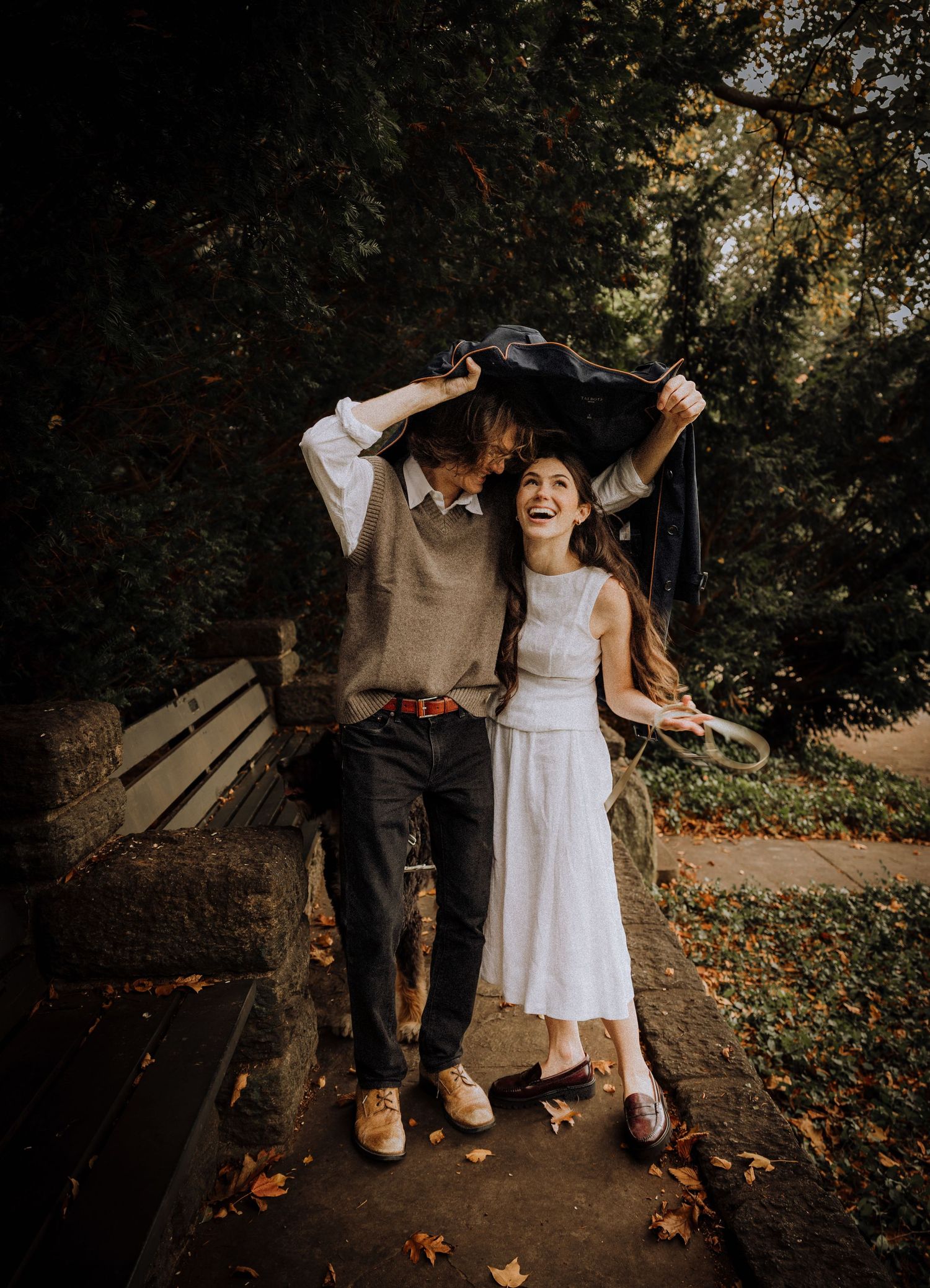 Playful autumn scene in a park with people enjoying fallen leaves on a pathway.