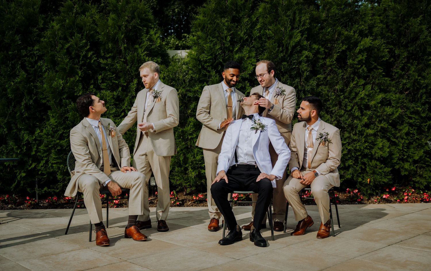 A group in beige suits and brown dress shoes sit casually on outdoor stone steps during a summer event.