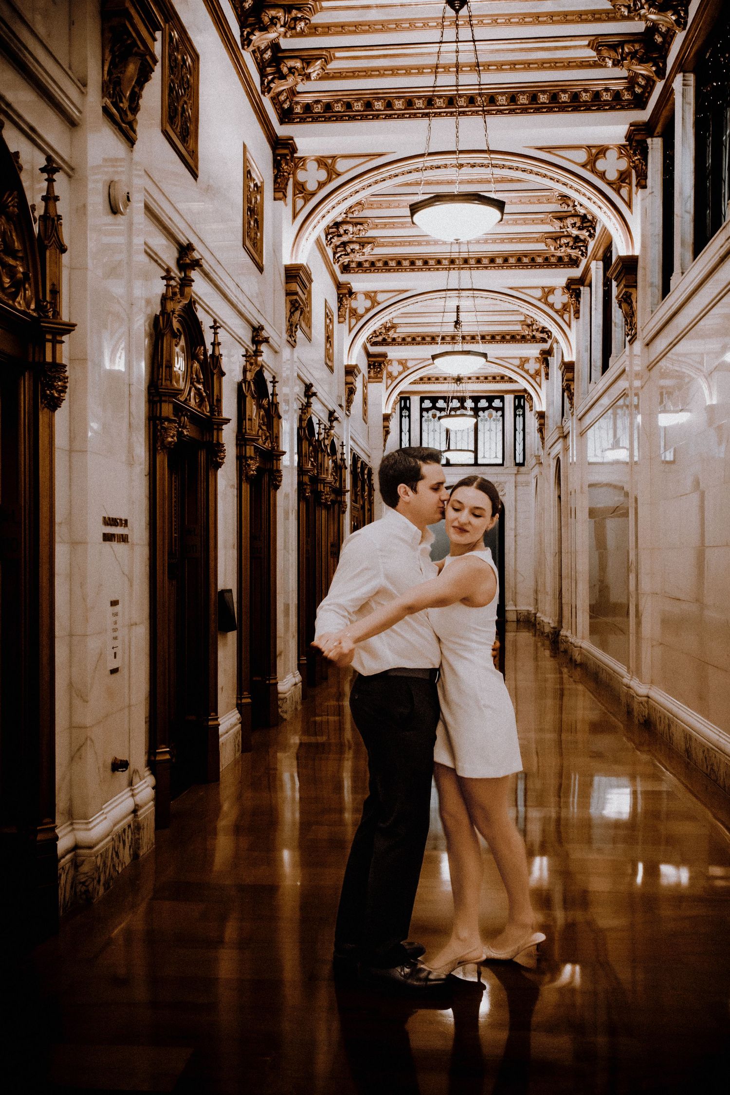 Romantic dance pose in a grand corridor with ornate architectural details and arched ceilings.