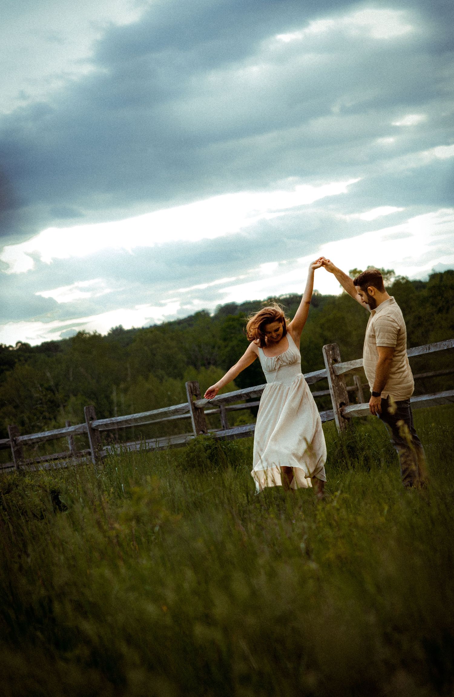 Dancing couple in a field with moody clouds overhead.