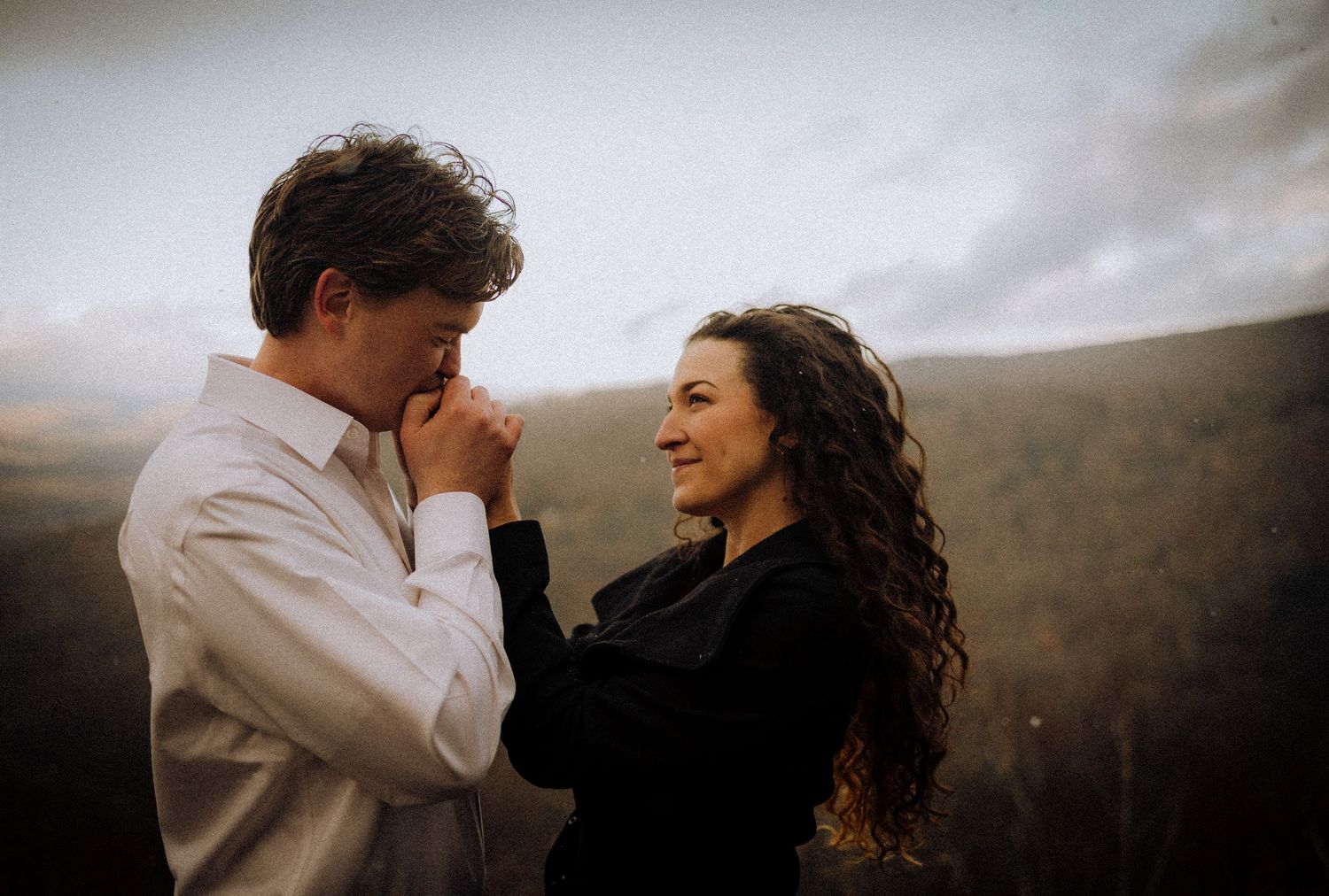 A couple shares an intimate moment against a misty mountain backdrop at sunset.