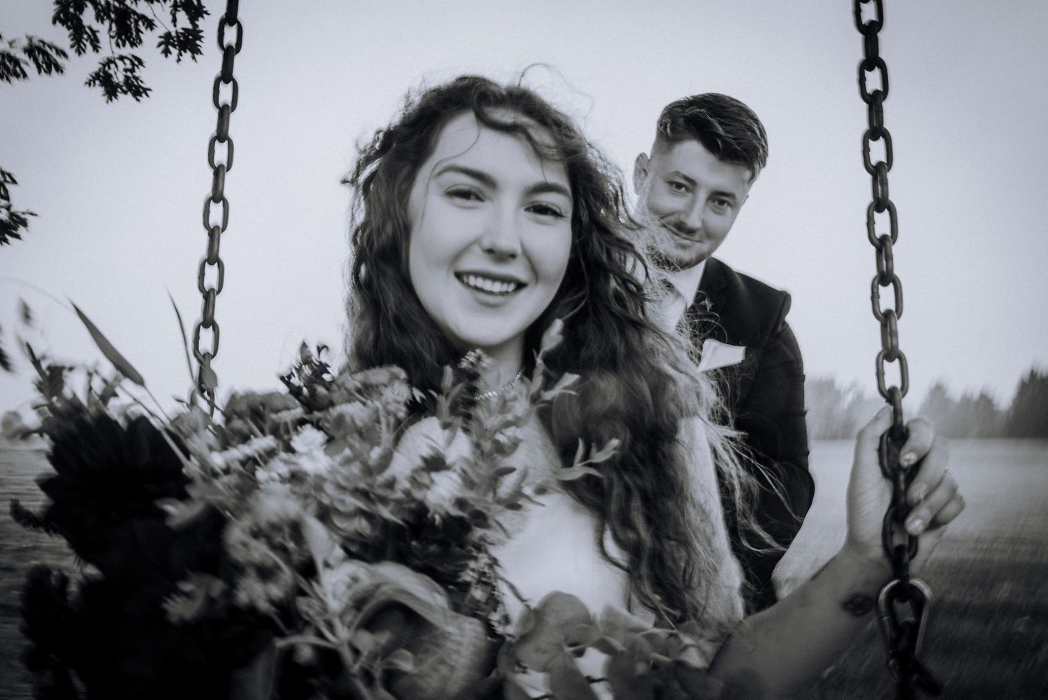 Couple shares playful moments on a swing set during wedding photoshoot.