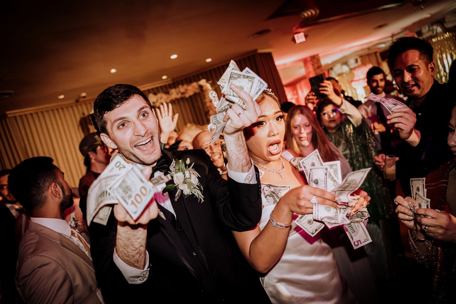 Partygoers on a dance floor waving and dancing with dollar bills in their hands during a celebration.