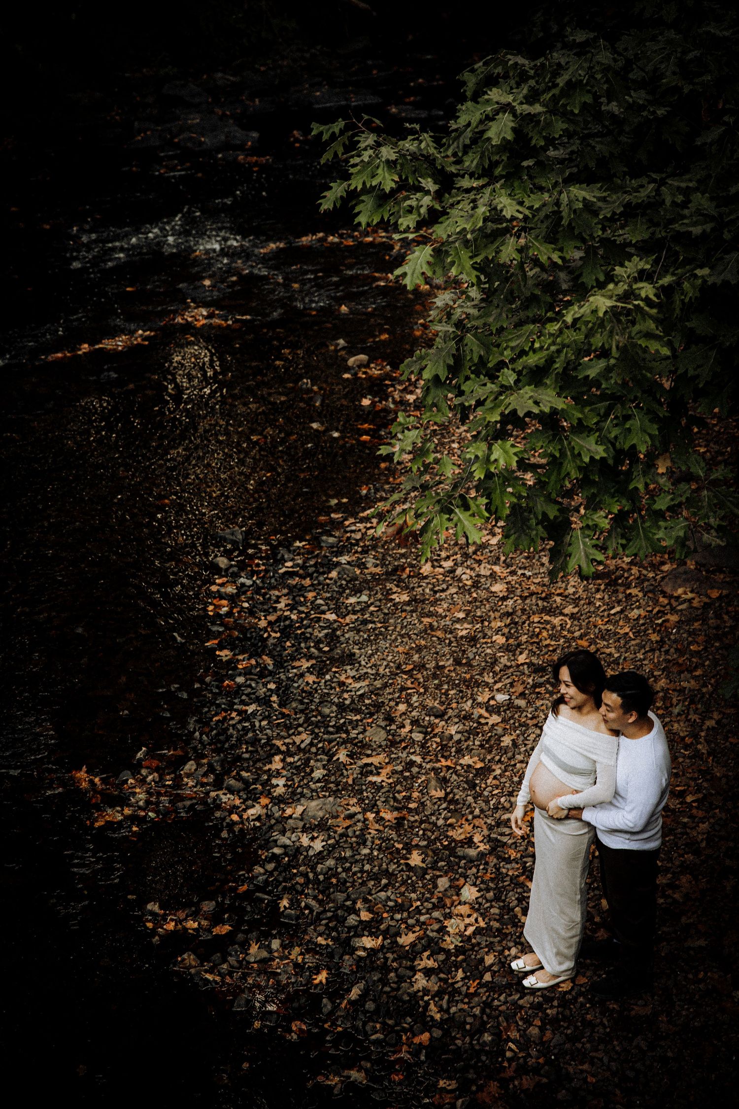Overhead view of couple embracing on fallen leaves in a dark wooded setting.