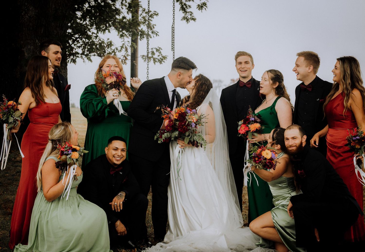 Wedding party members in red and black attire gather outdoors for candid group photos during a celebration.