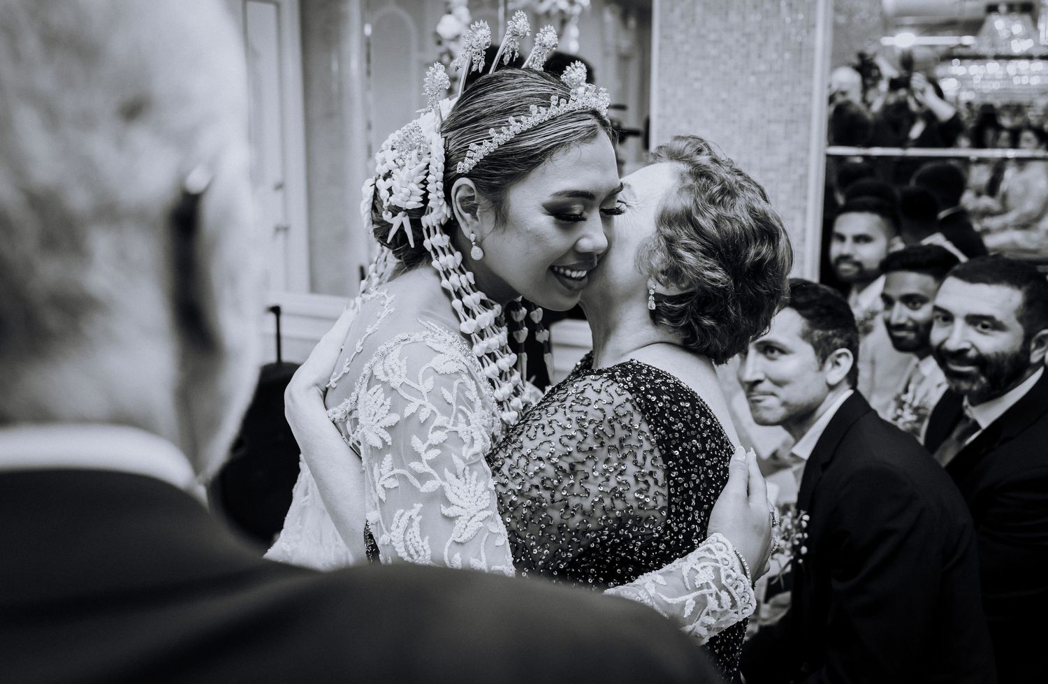 A black and white wedding photo sequence showing an intimate first kiss between newlyweds surrounded by guests.