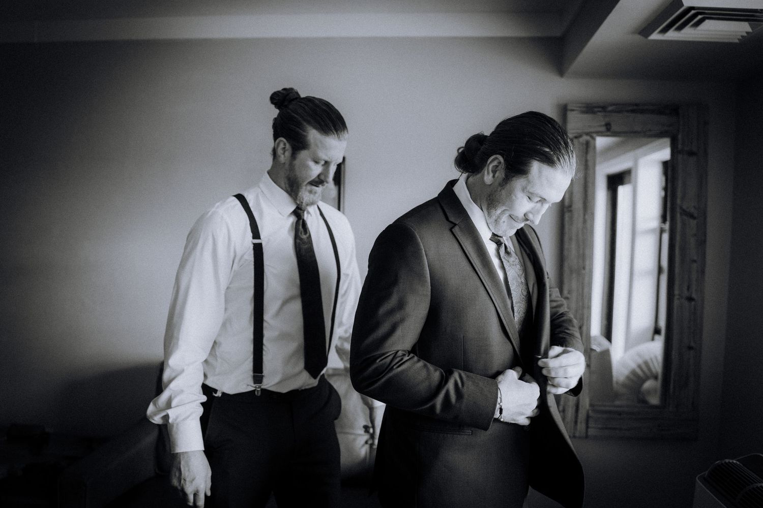 Groomsmen in suits and ties preparing for a wedding ceremony in a dimly lit hallway.