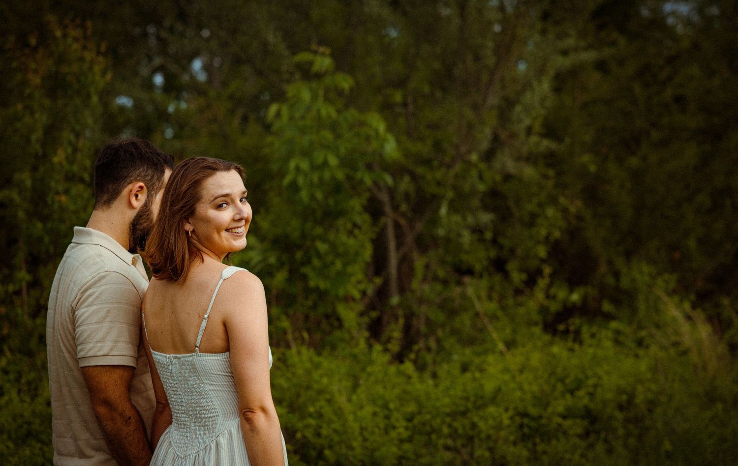 Couple embracing in a romantic outdoor setting with lush greenery.
