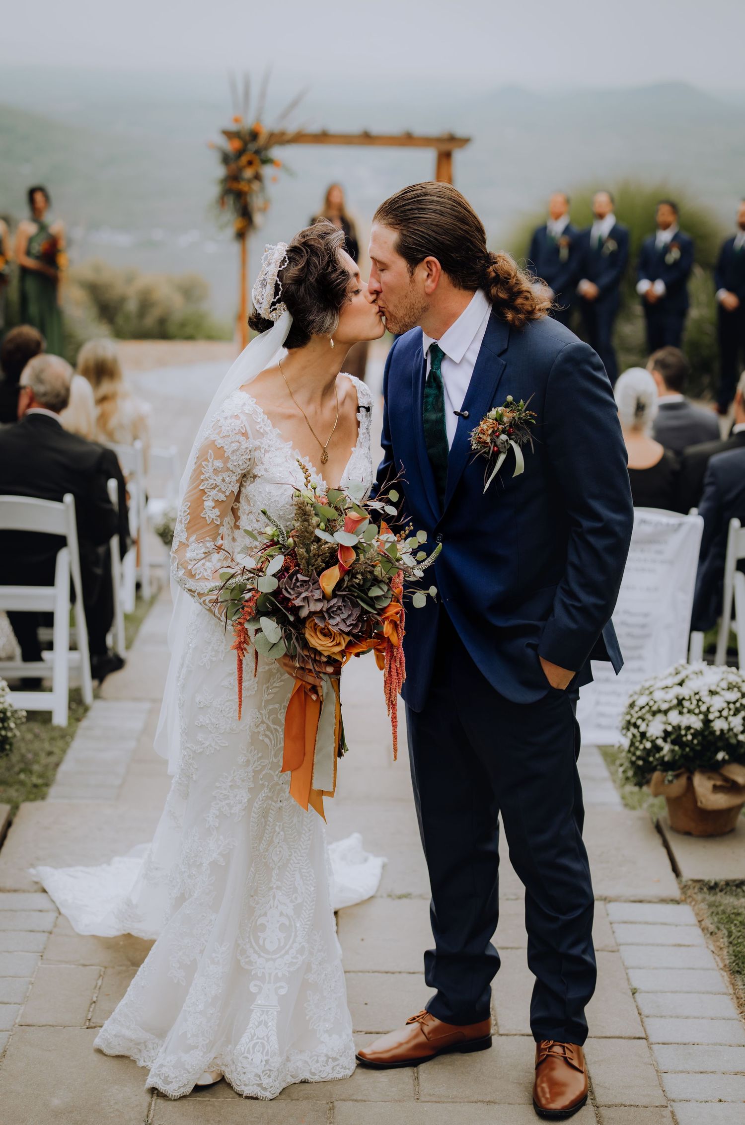 Wedding couple embraces on stone terrace with mountain vista and floral decorations.