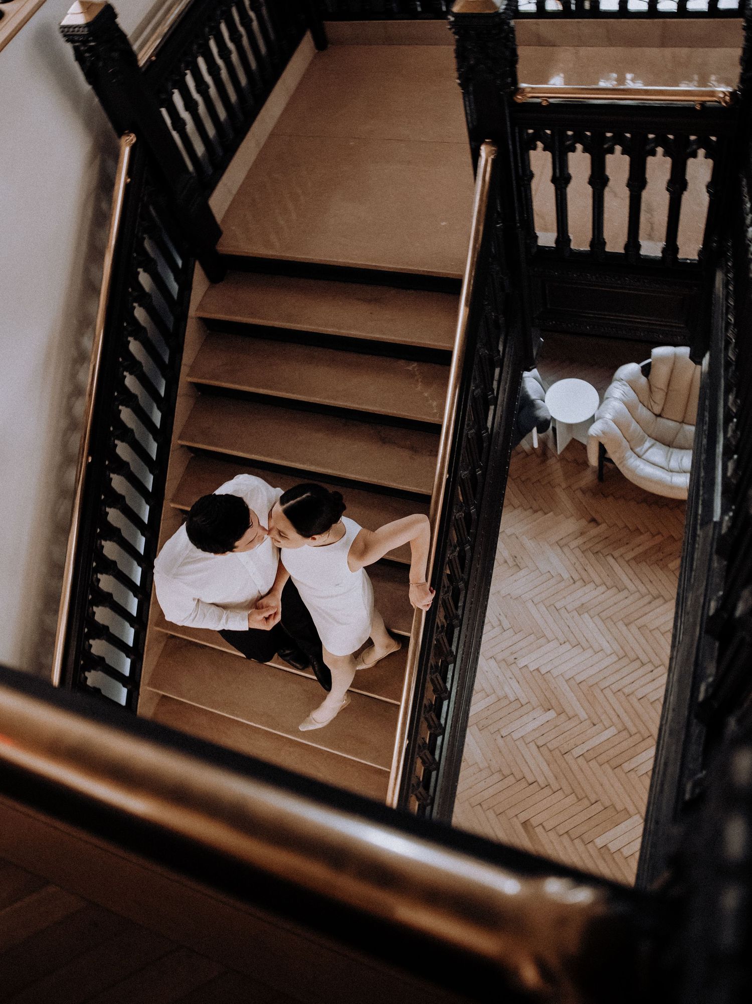 A couple in formal attire shares an intimate moment on a staircase in moody lighting.