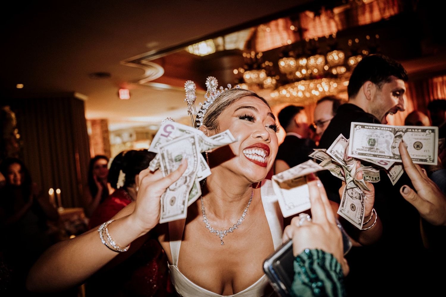 Partygoer joyfully holds cash money at a dimly lit nightclub celebration with others in background.